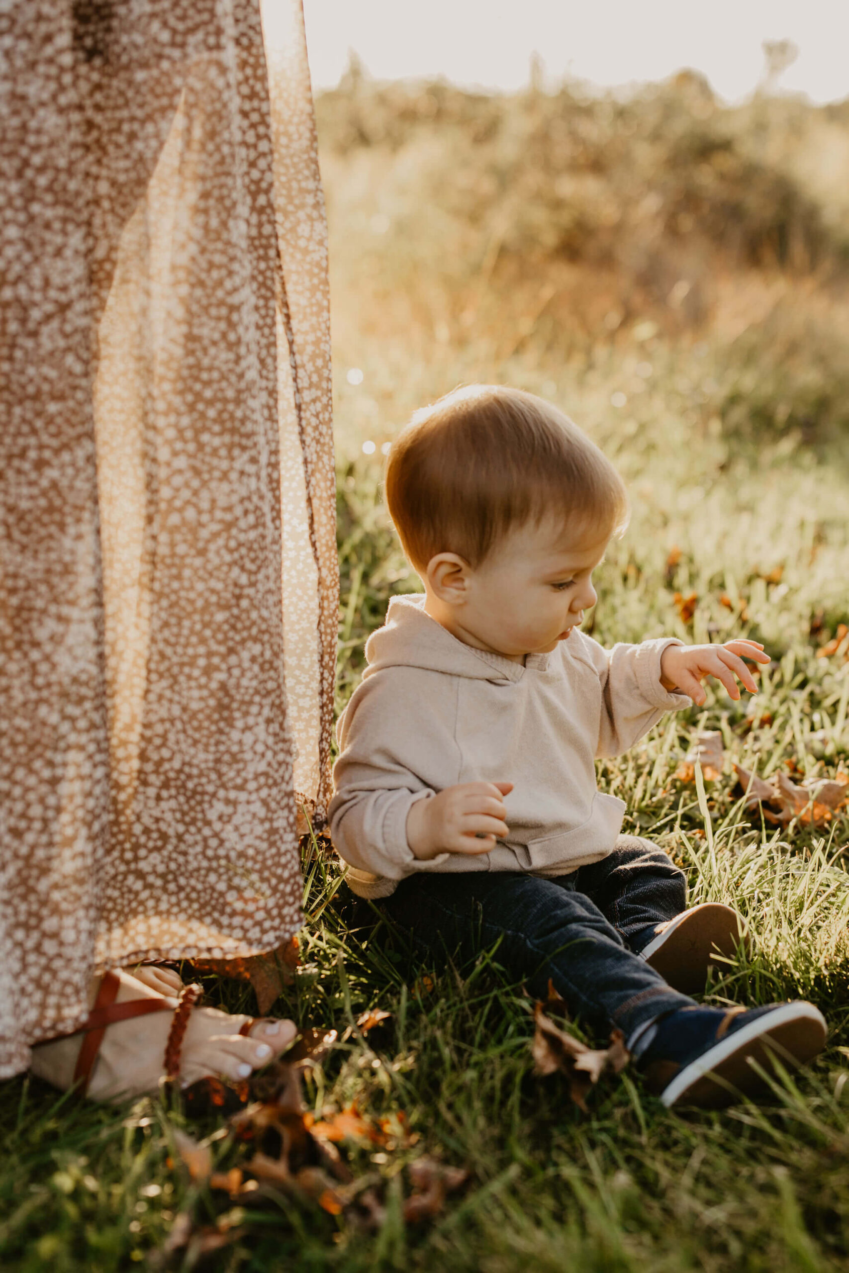 a young boy playing with cut grass at his mother's feet during sunset