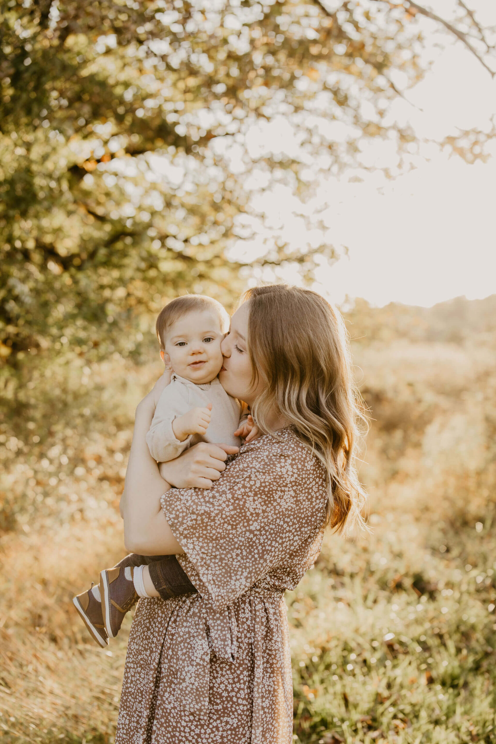 a mother kissing her young son on the cheek during sunset