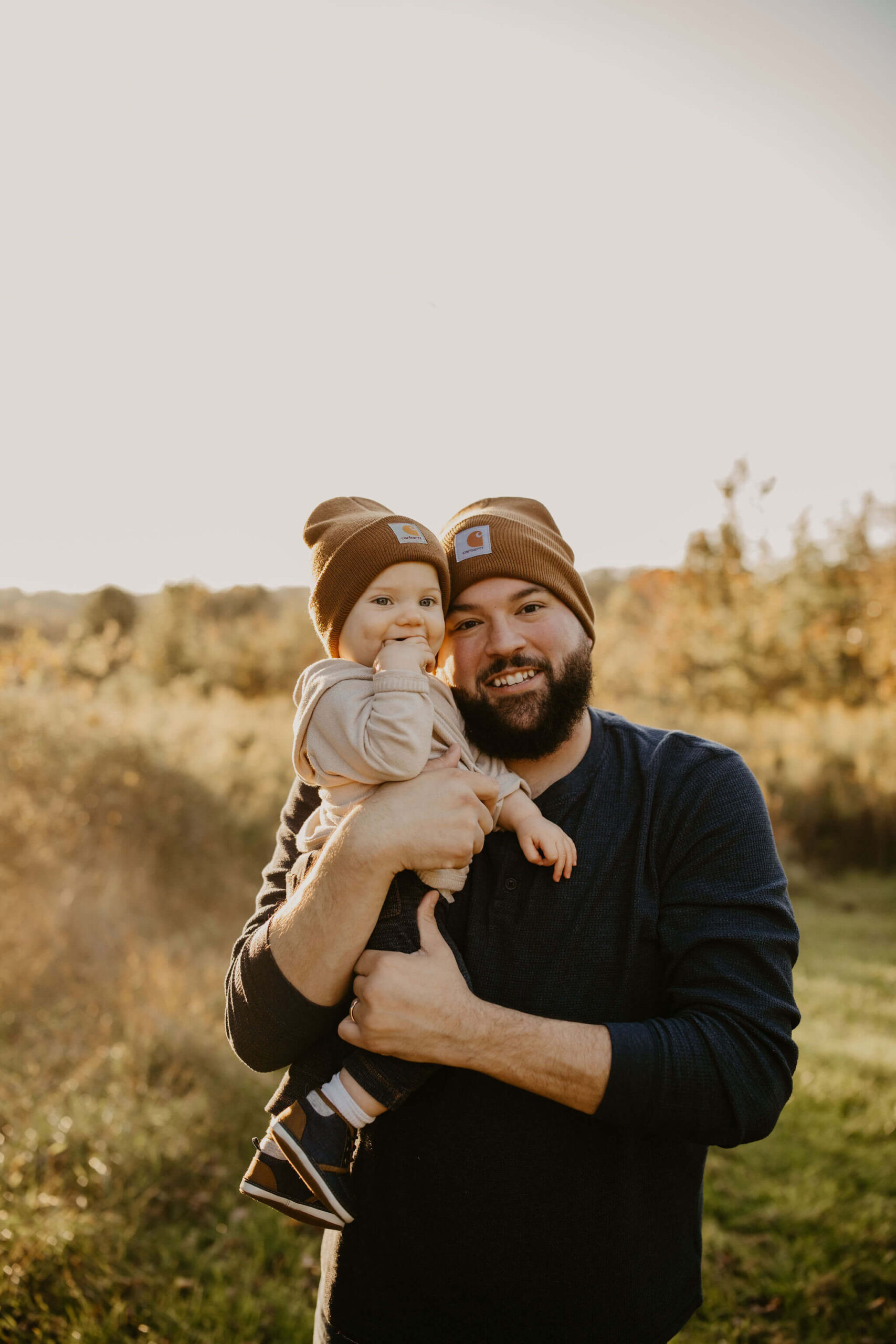 a father holding his young son, both wearing matching brown carhart hats