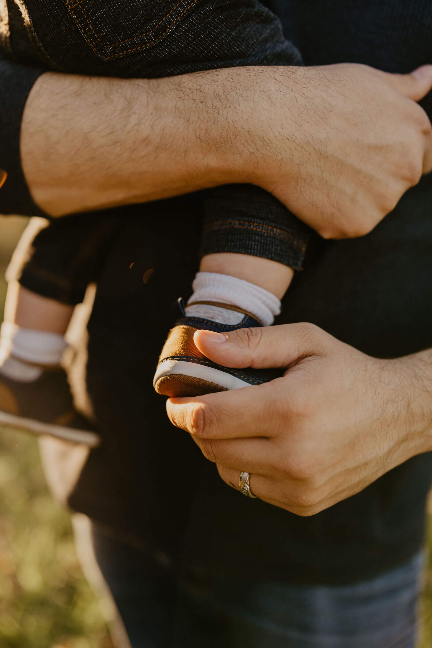 a father holding his infant son's feet. his wedding band is visible.