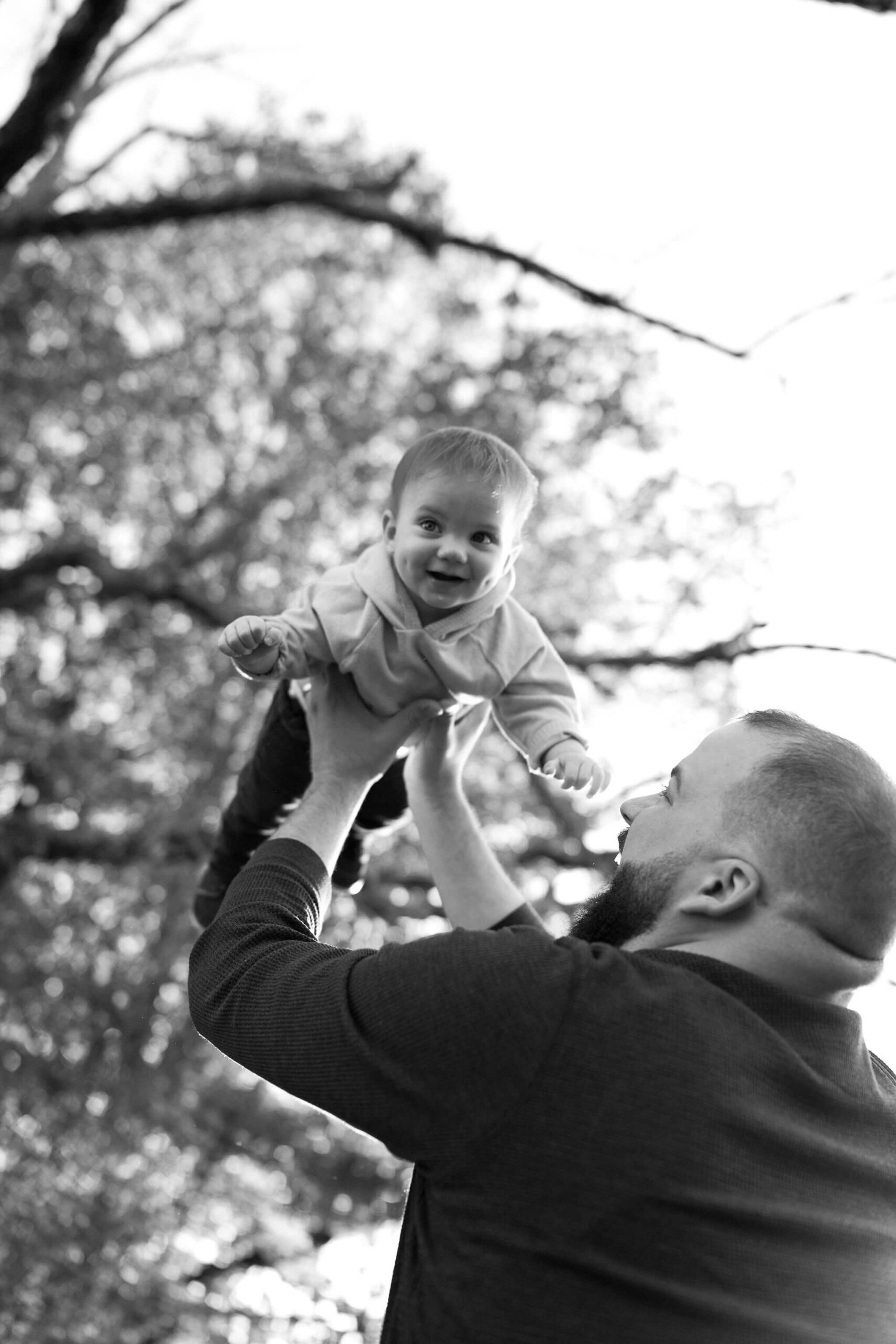 a black and white image of a dad throwing his son in the air, who is smiling off camera