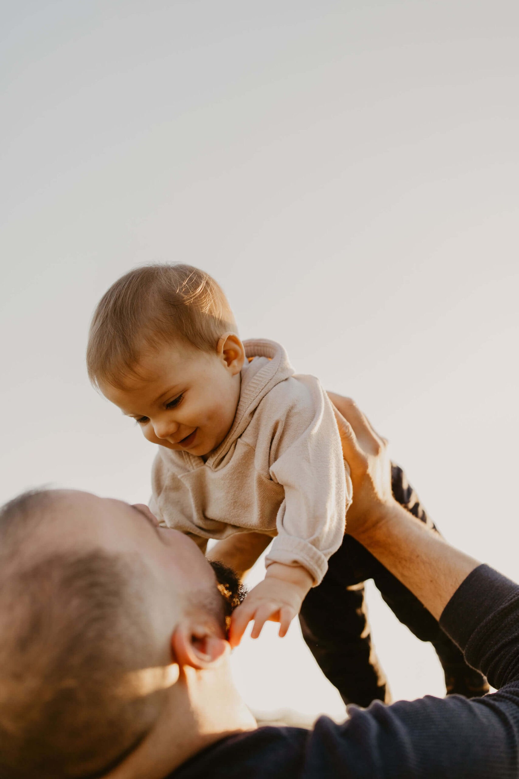 a father holding his son above his head in the air, both smiling at each other