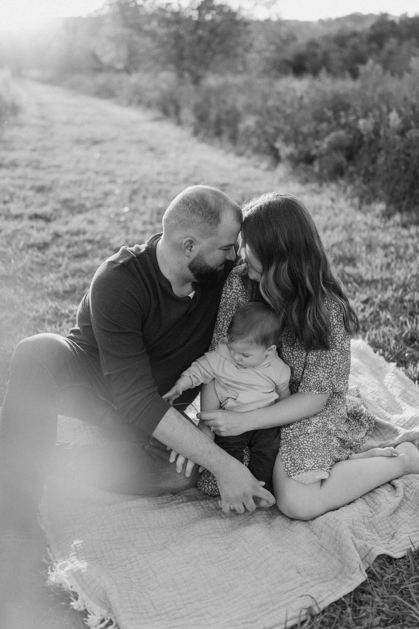 a family (father, mother, and son) sitting and embracing on a picnic blanket