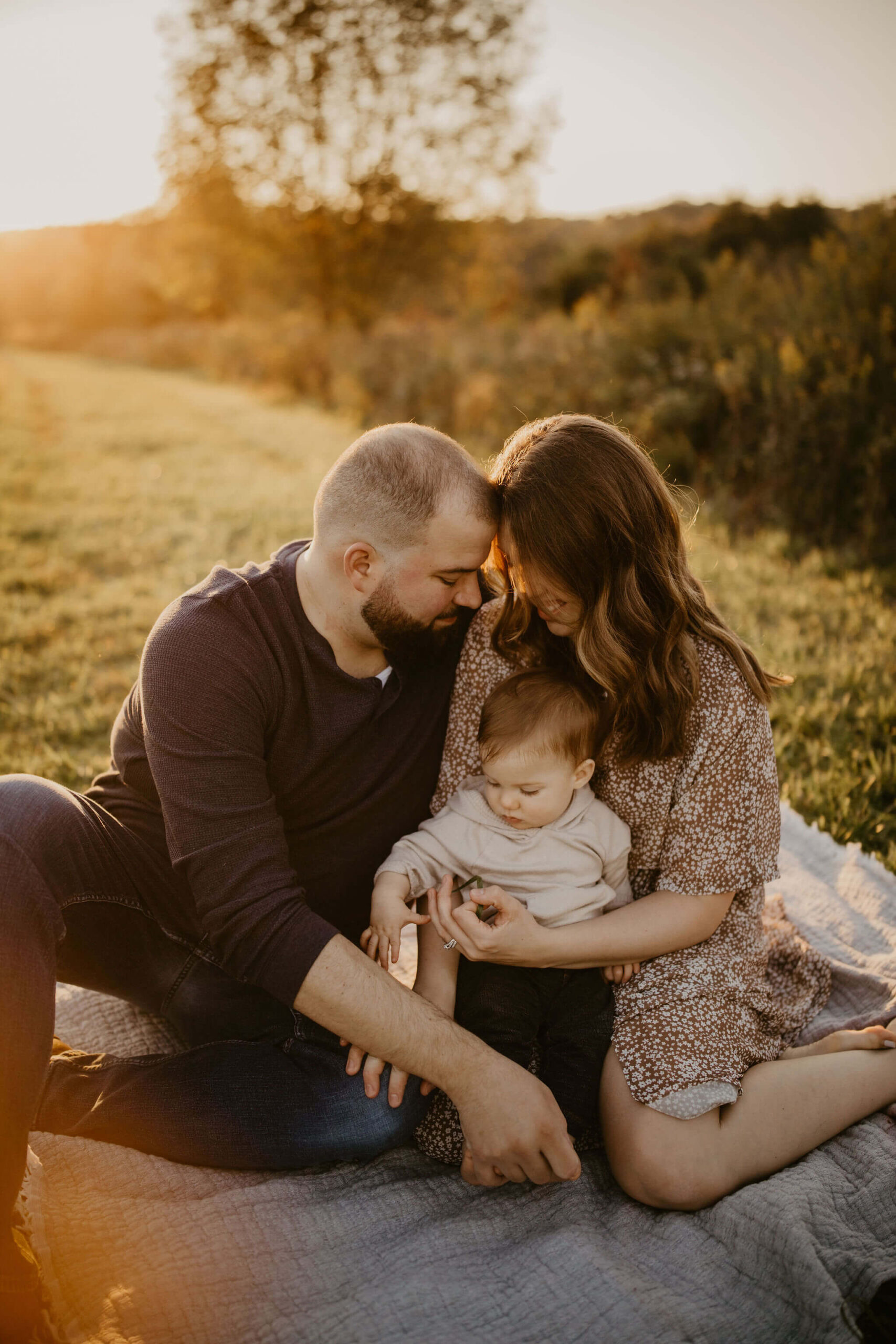 a family (father, mother, and son) sitting and embracing on a picnic blanket