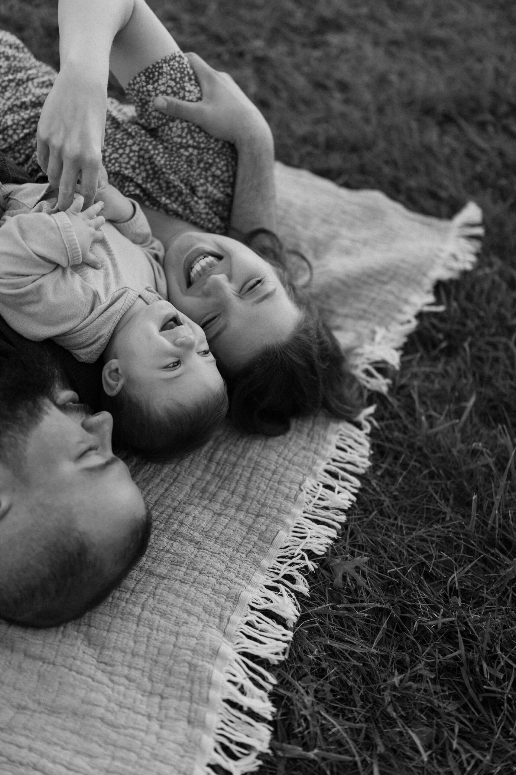 a family (father, mother, son) laying on a picnic blanket, cuddling together and laughing