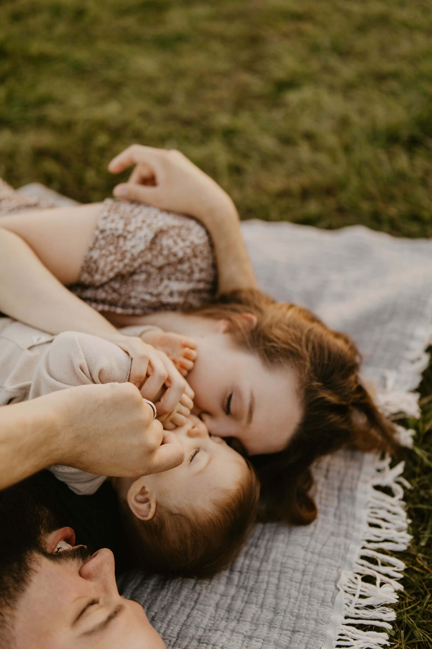 a family (father, mother, son) laying on a picnic blanket, cuddling together and laughing