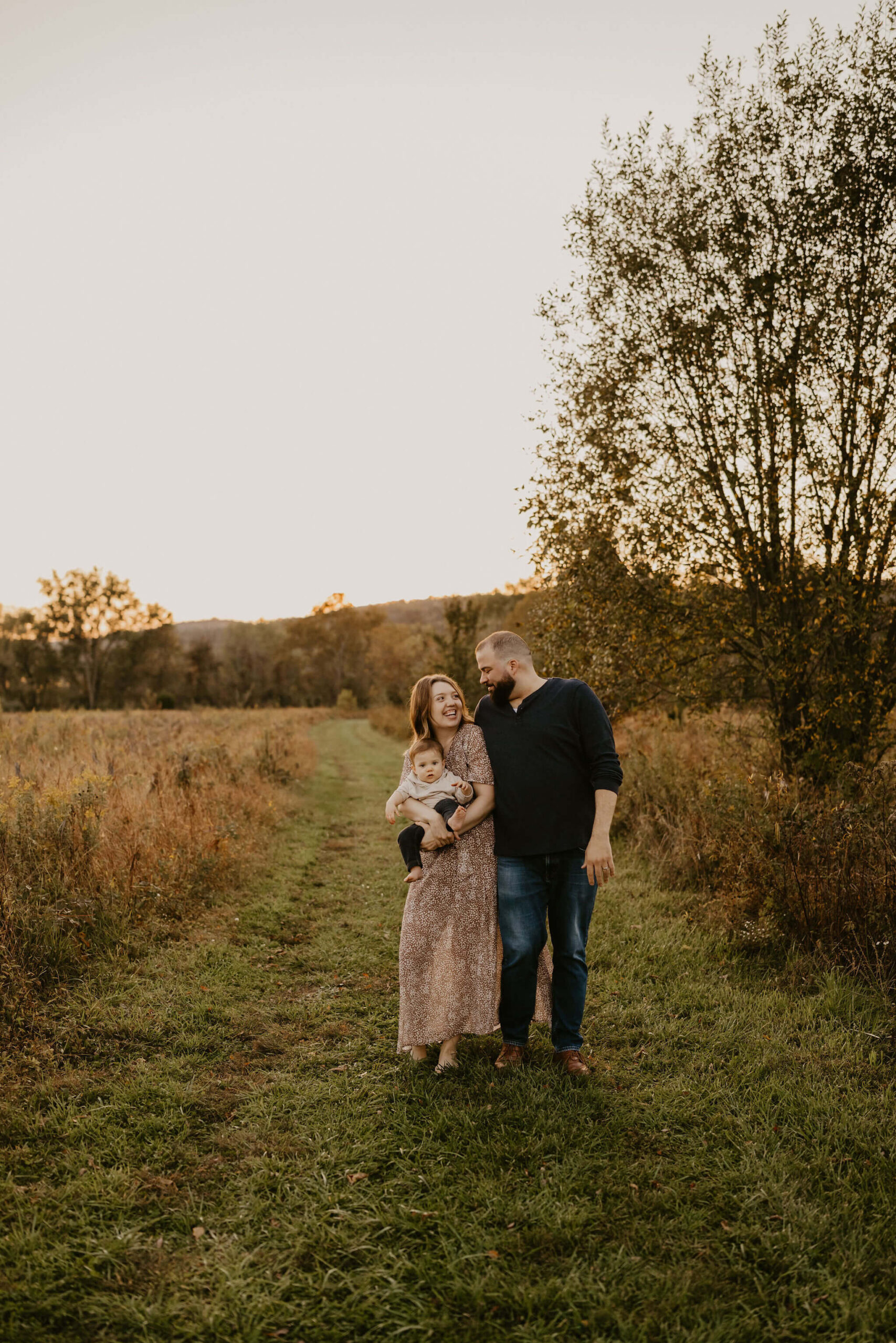 a family (mother, father, and son) walking toward the camera through a field at sunset. 