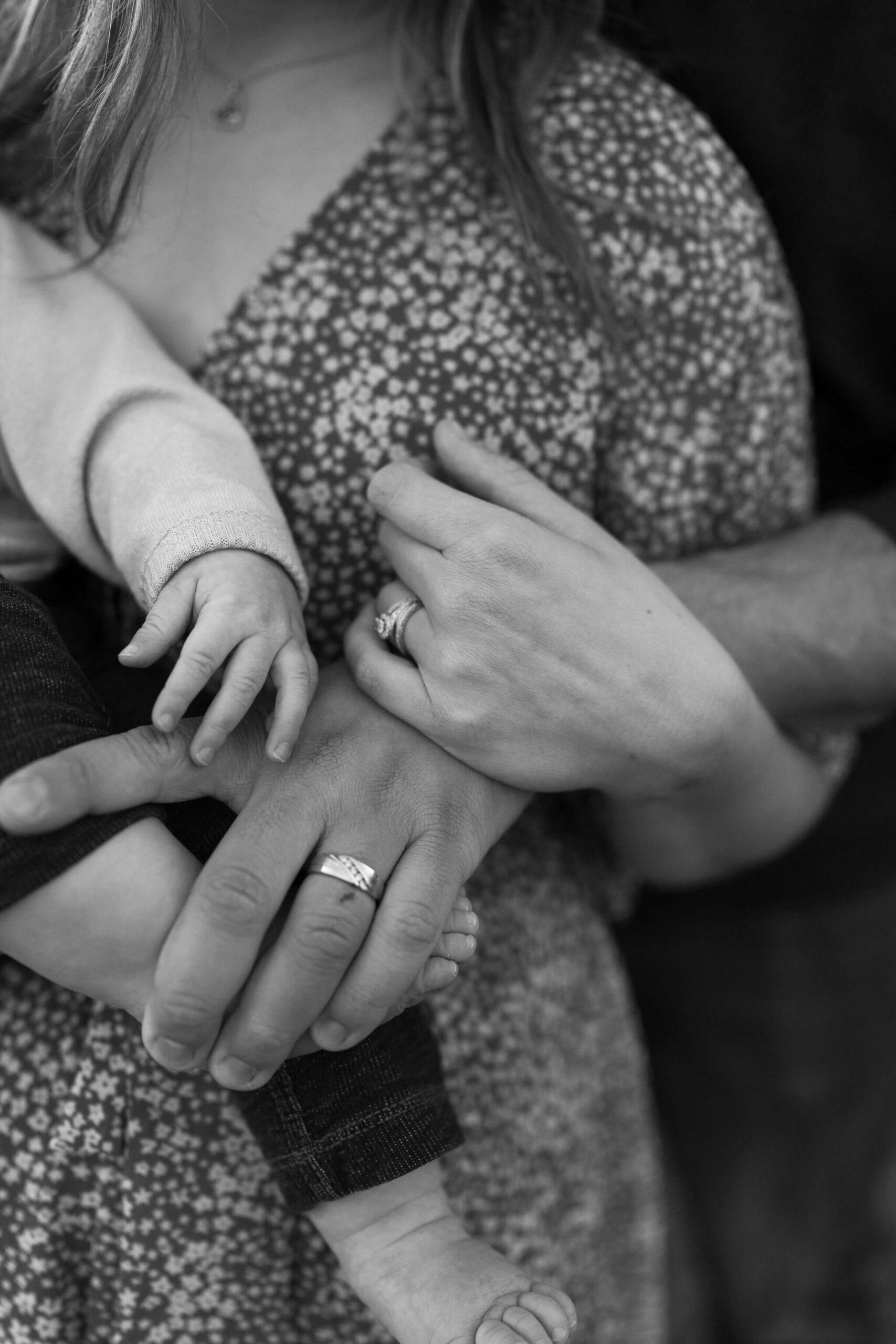 black and white close up image of hands: a mother and father, both with their wedding rings, and their young son