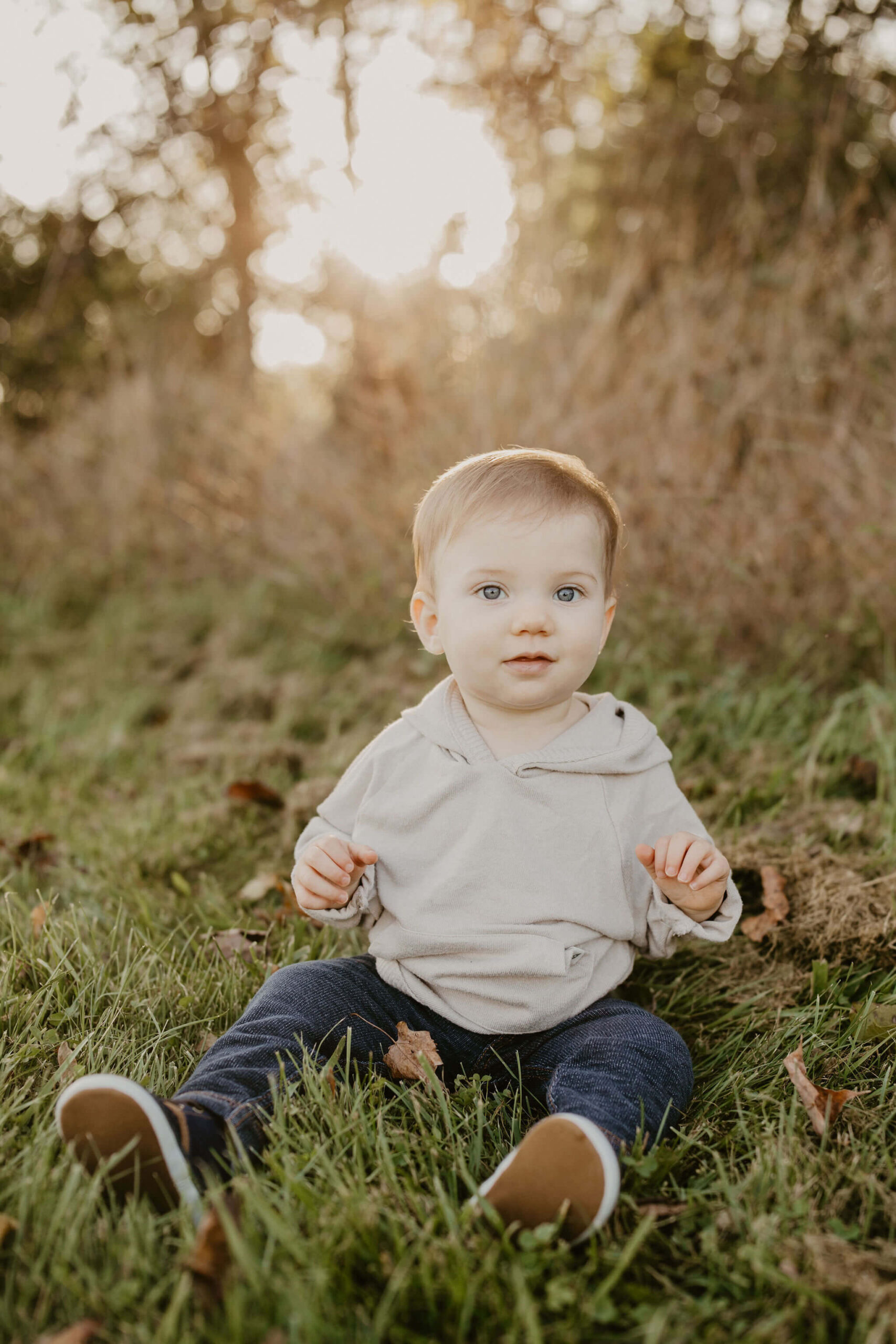 a little boy sitting in a field, playing. He is looking directly at the camera with a soft smile.