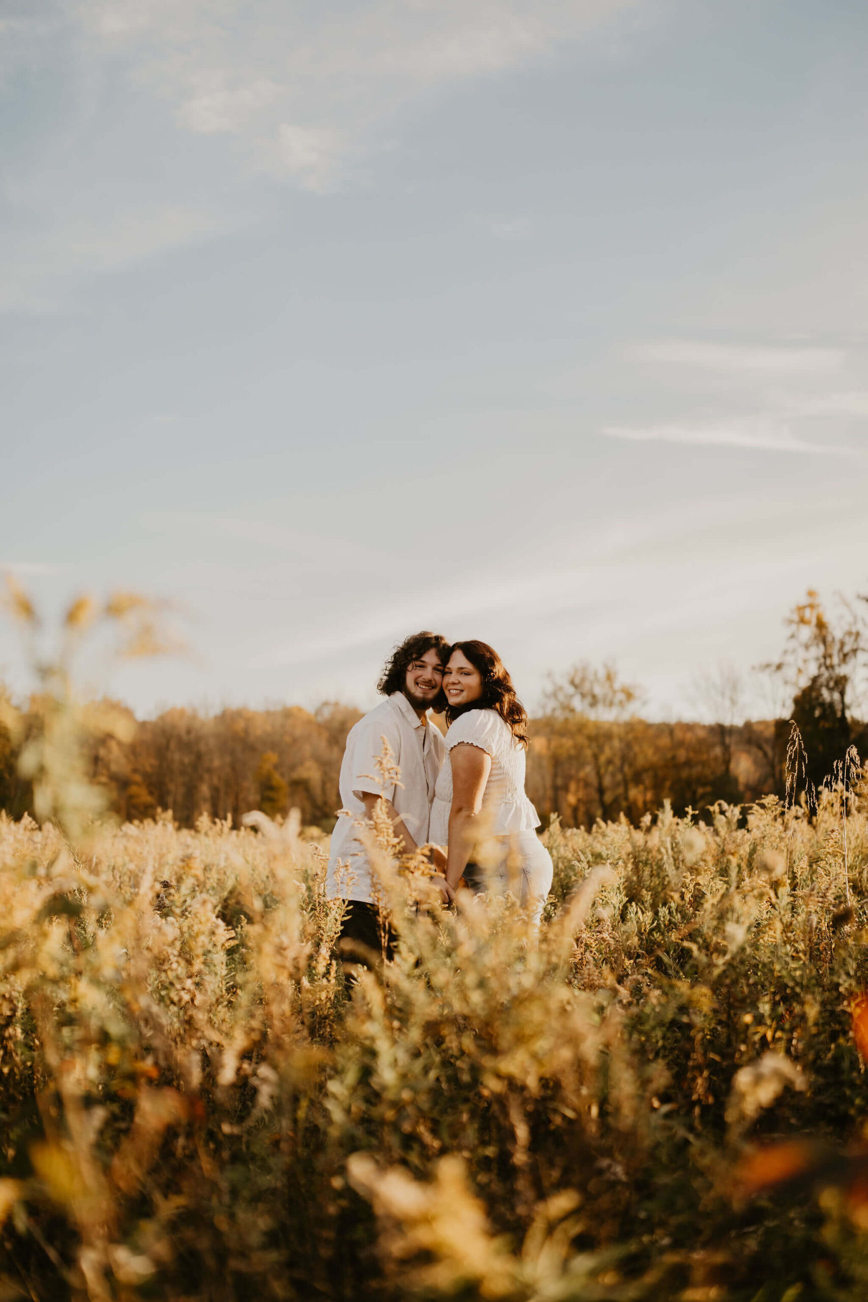 a boy and a girl with long brown hair posing cheek-to-cheek for a photograph in a golden field during fall