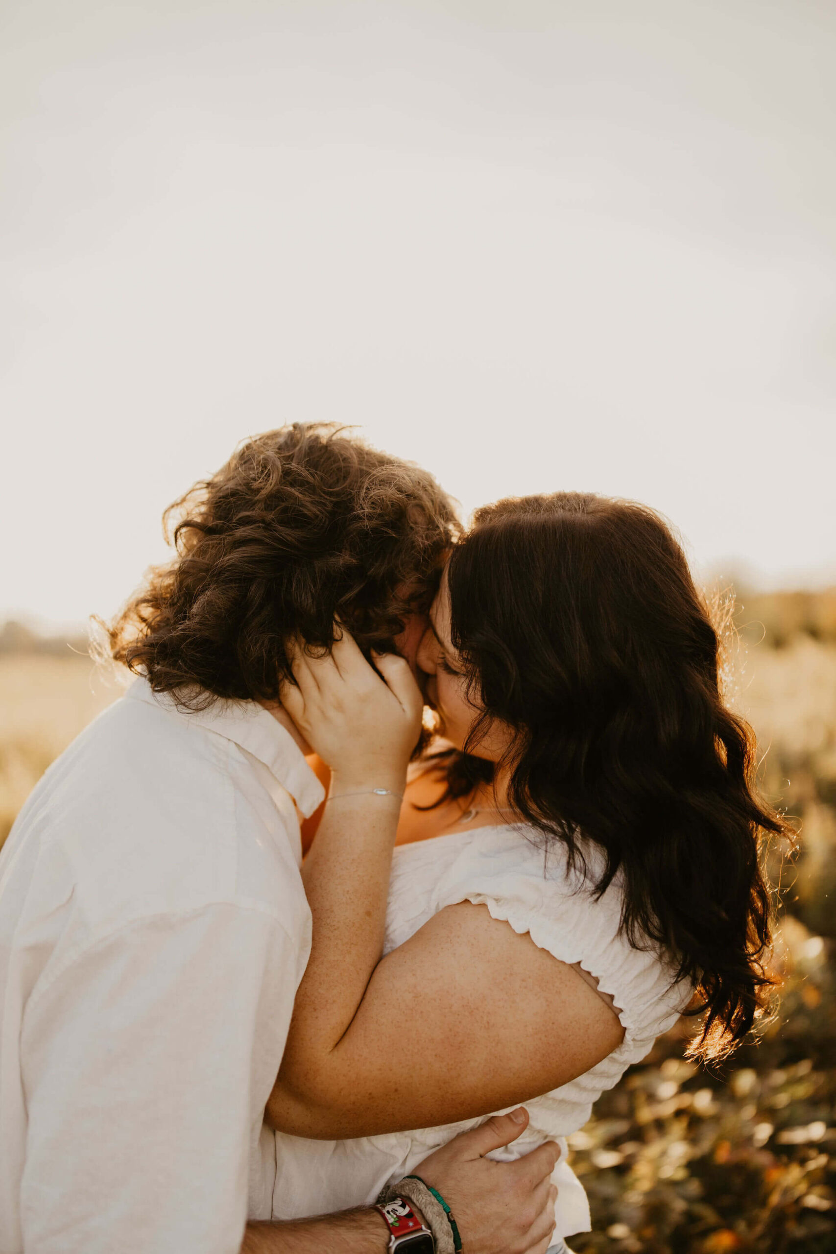 a boy and a girl kissing, both with long brown hair and white shirts at sunset