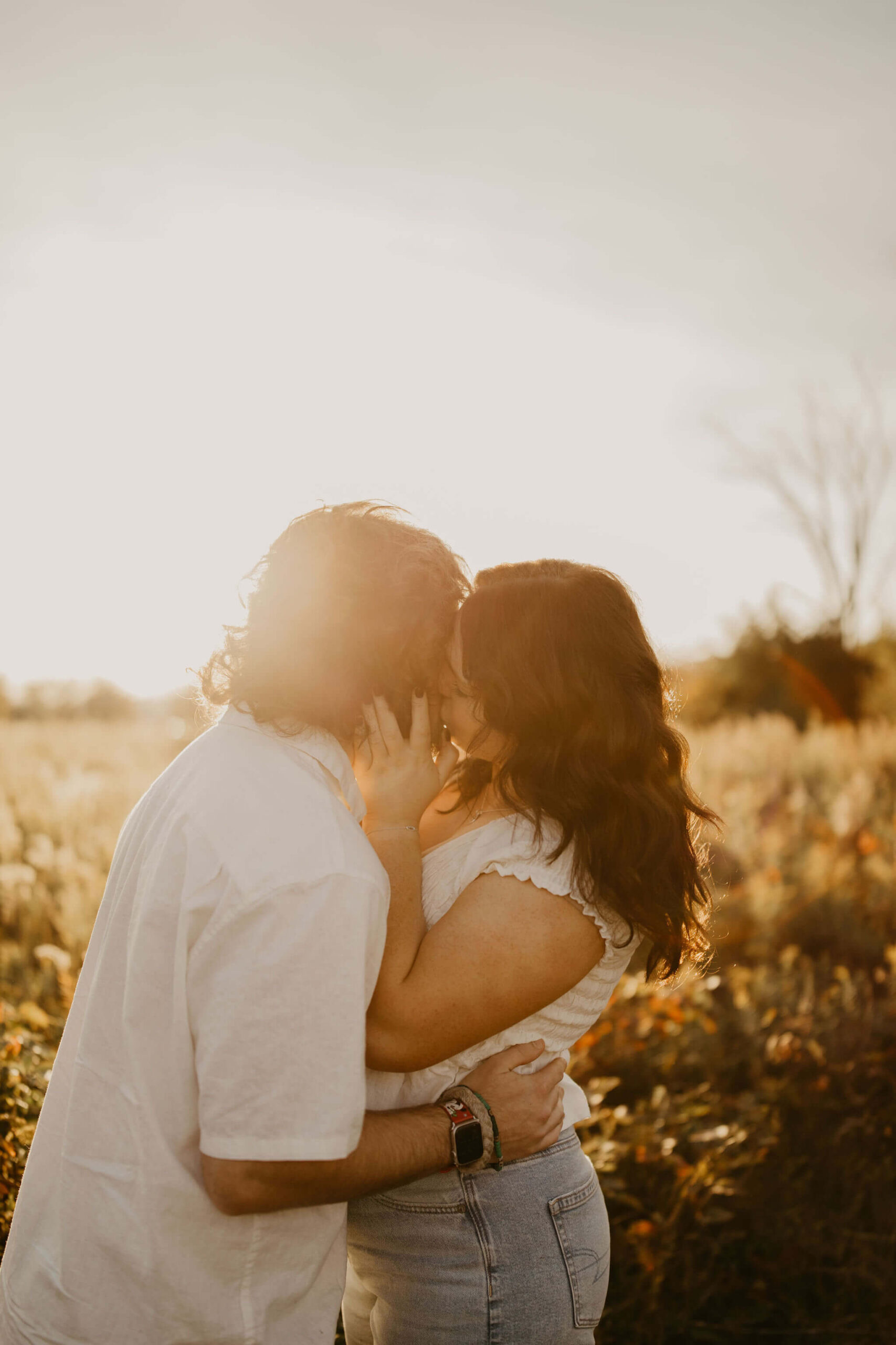 a couple embracing and kissing in a field at sunset