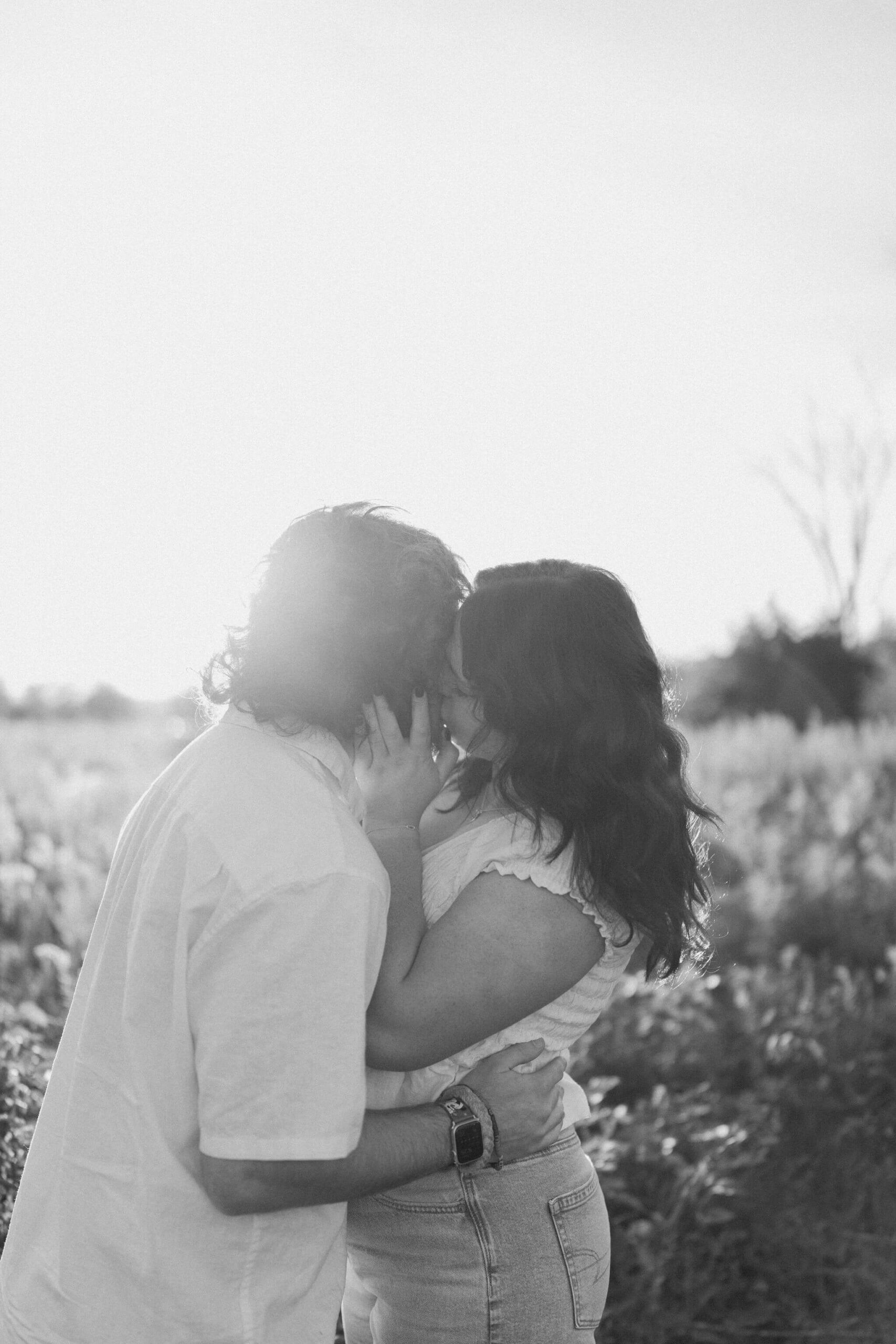 grainy black and white image of a boy and a girl kissing in a field