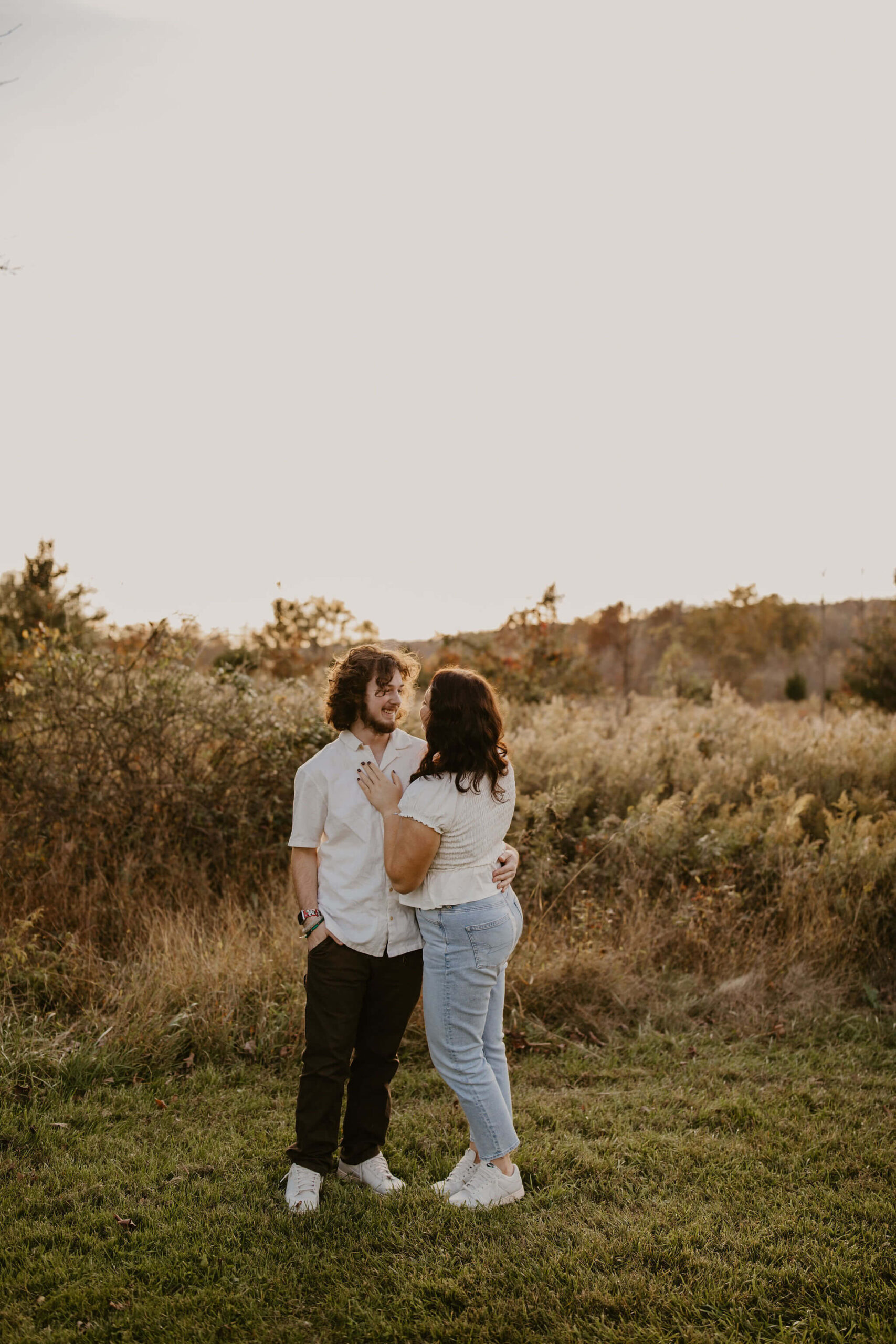 a boy and a girl posing for a photograph, looking at each other. Both have long brown hair and are wearing white shirts.