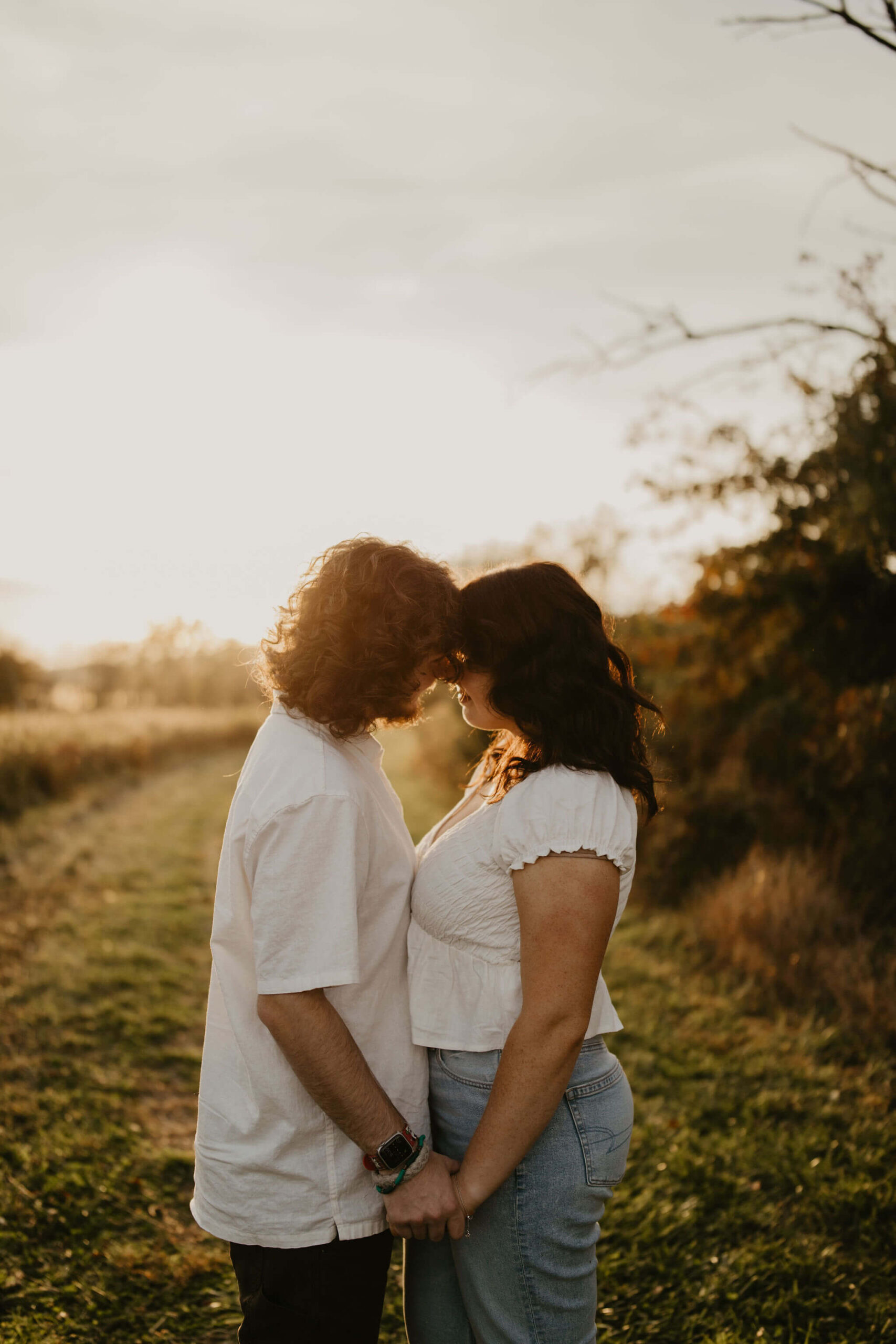 a young couple standing in a field, holding hands and touching foreheads