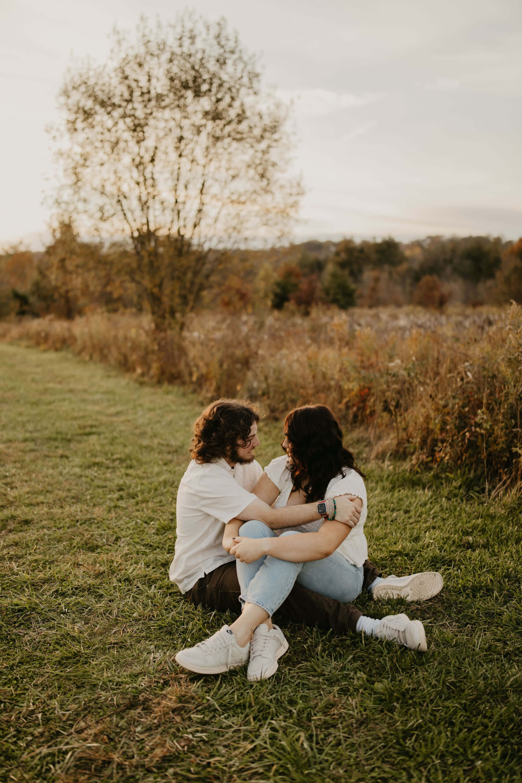 a couple sitting in a field at sunset, smiling at each other