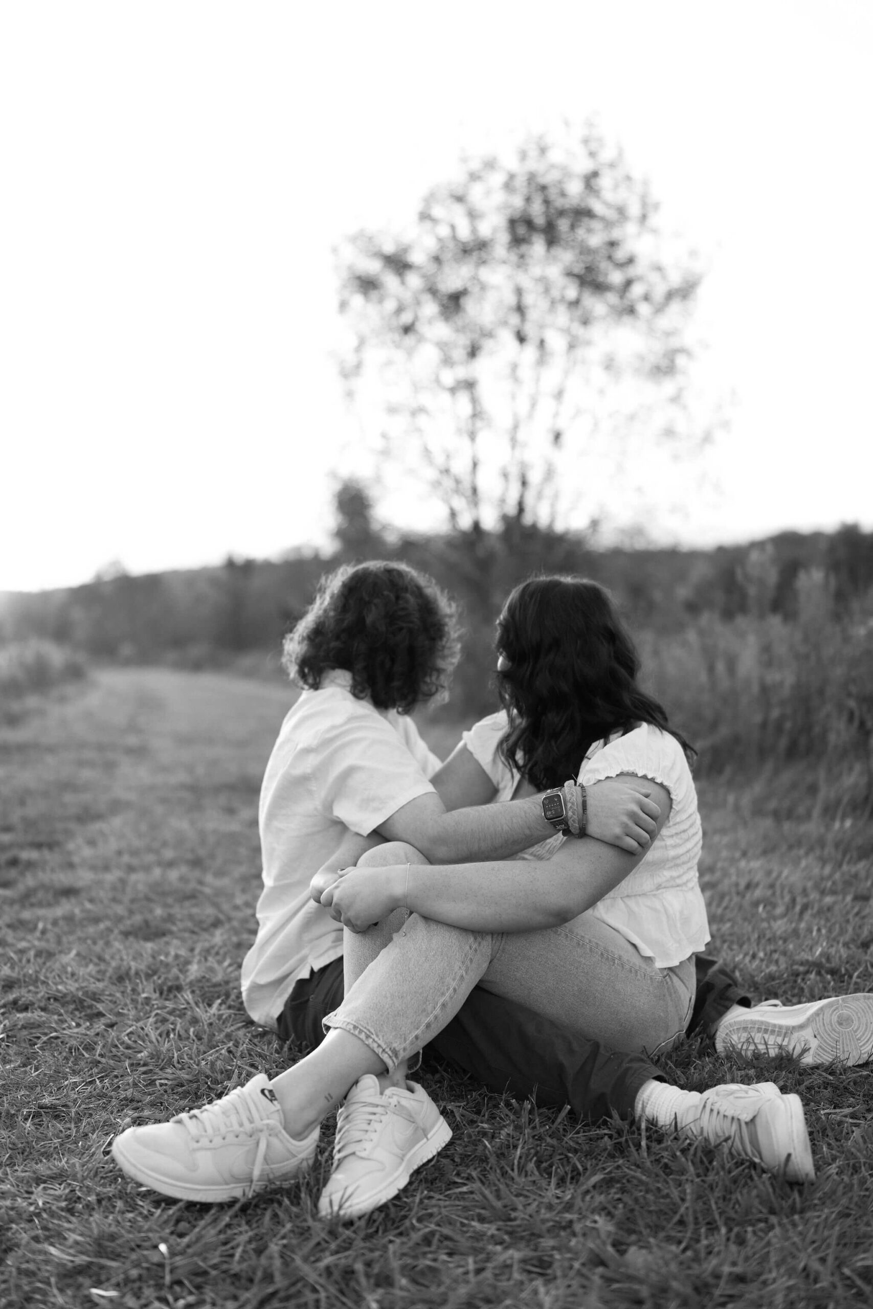 black and white image of a couple sitting in the field watching the sunset