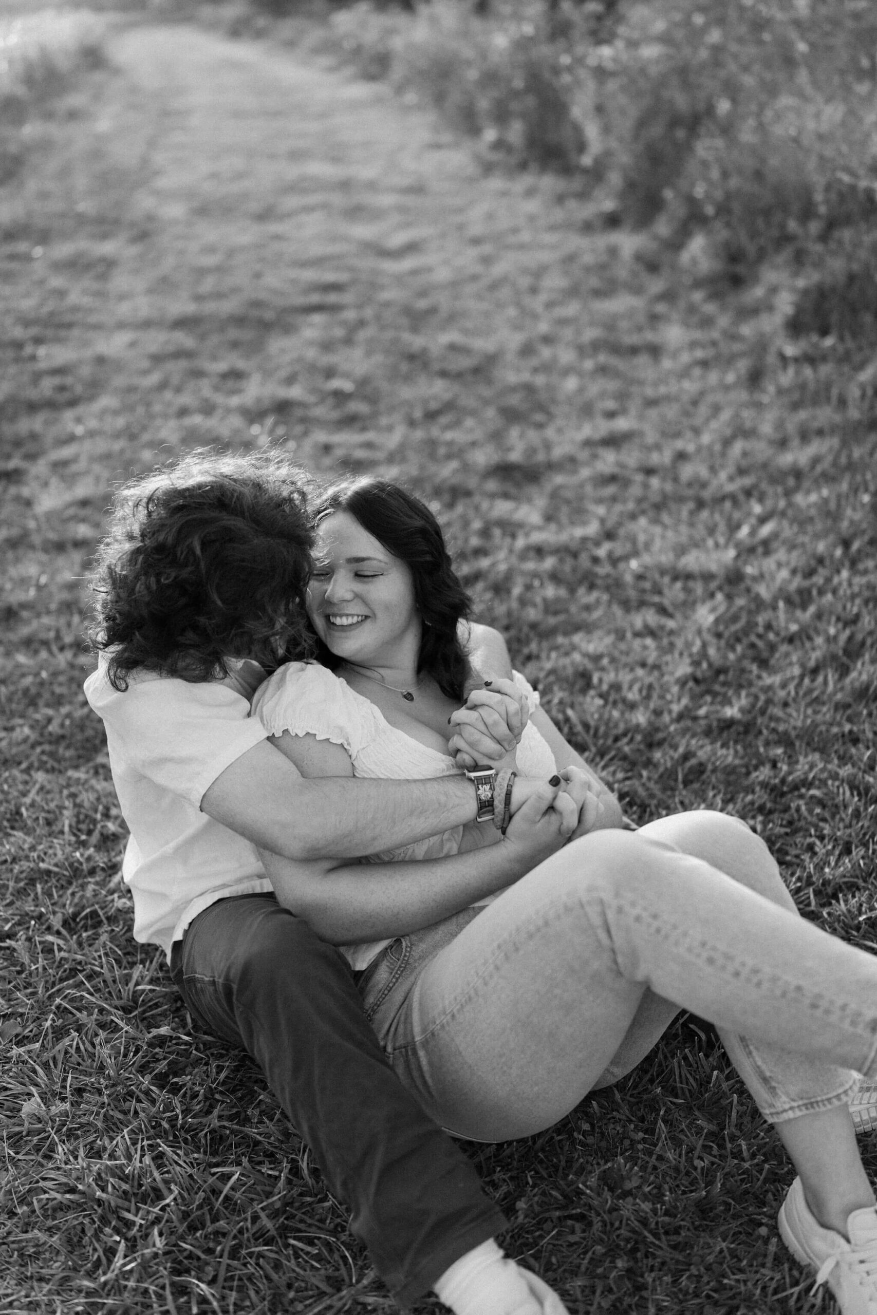 black and white image of a couple cuddling in a field, laughing