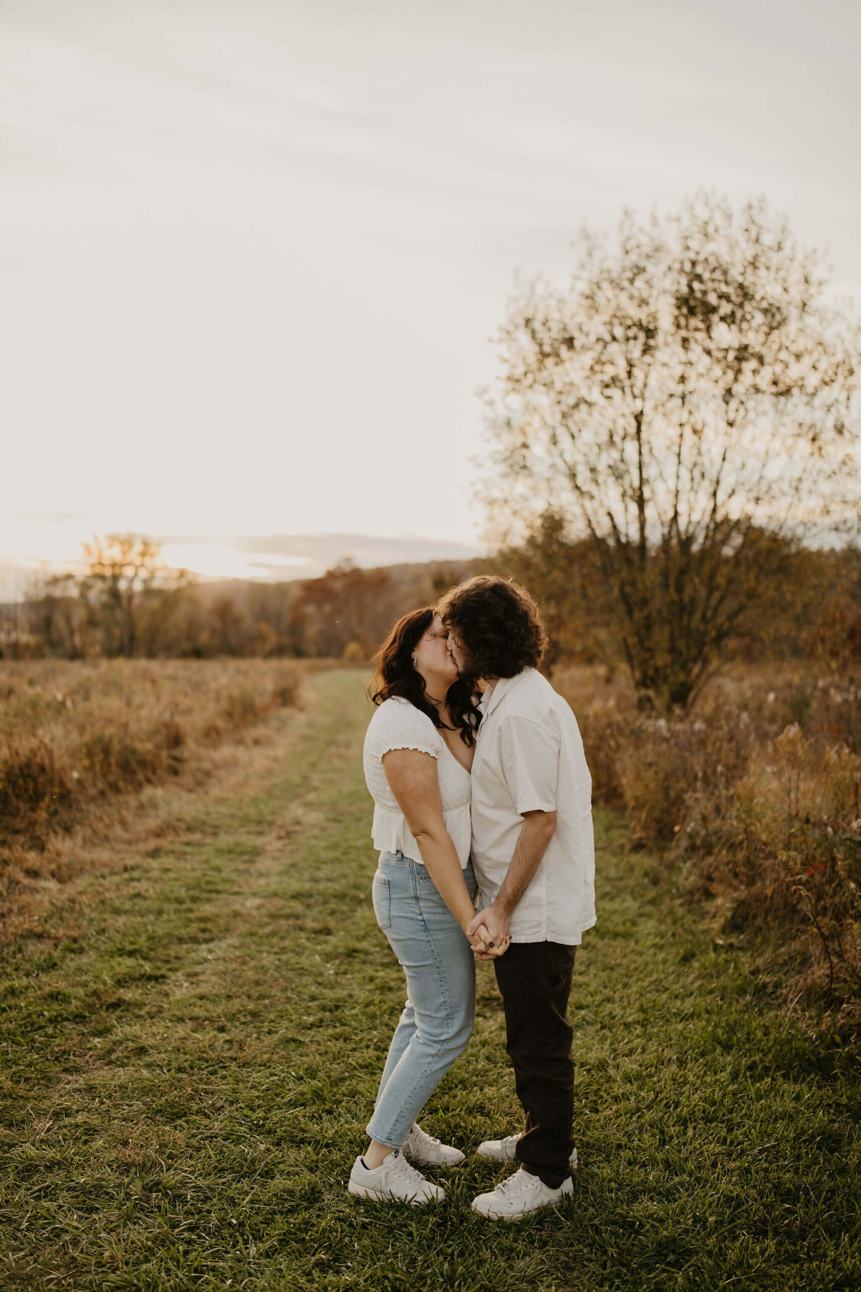 a young couple holding hands and kissing in a golden field at sunset