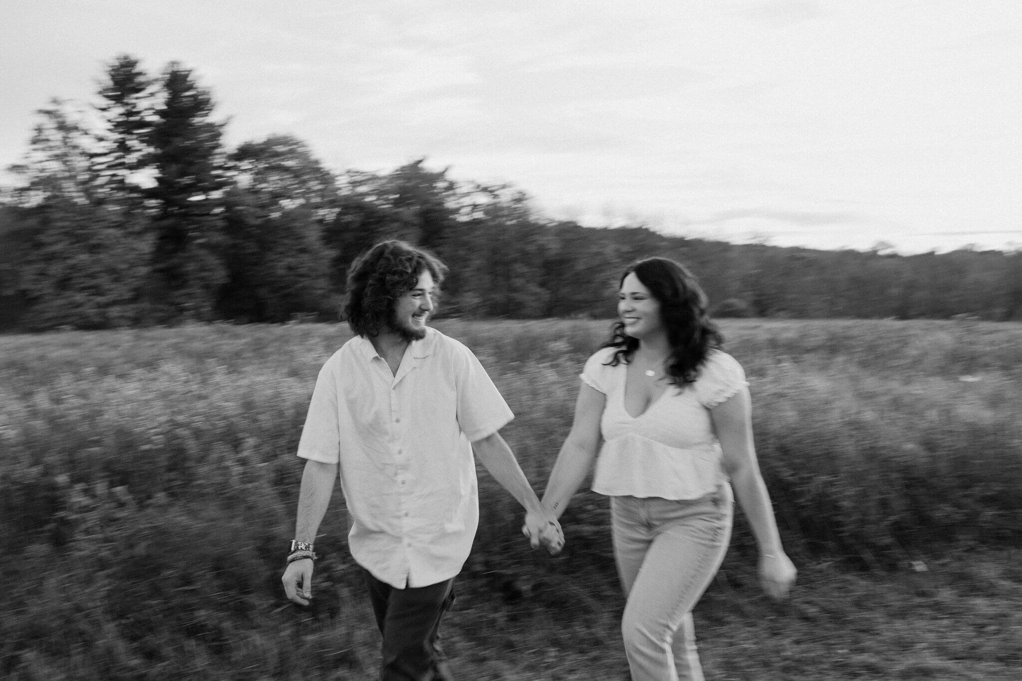 a motion-blur black and white image of a couple walking through a field, smiling at each other