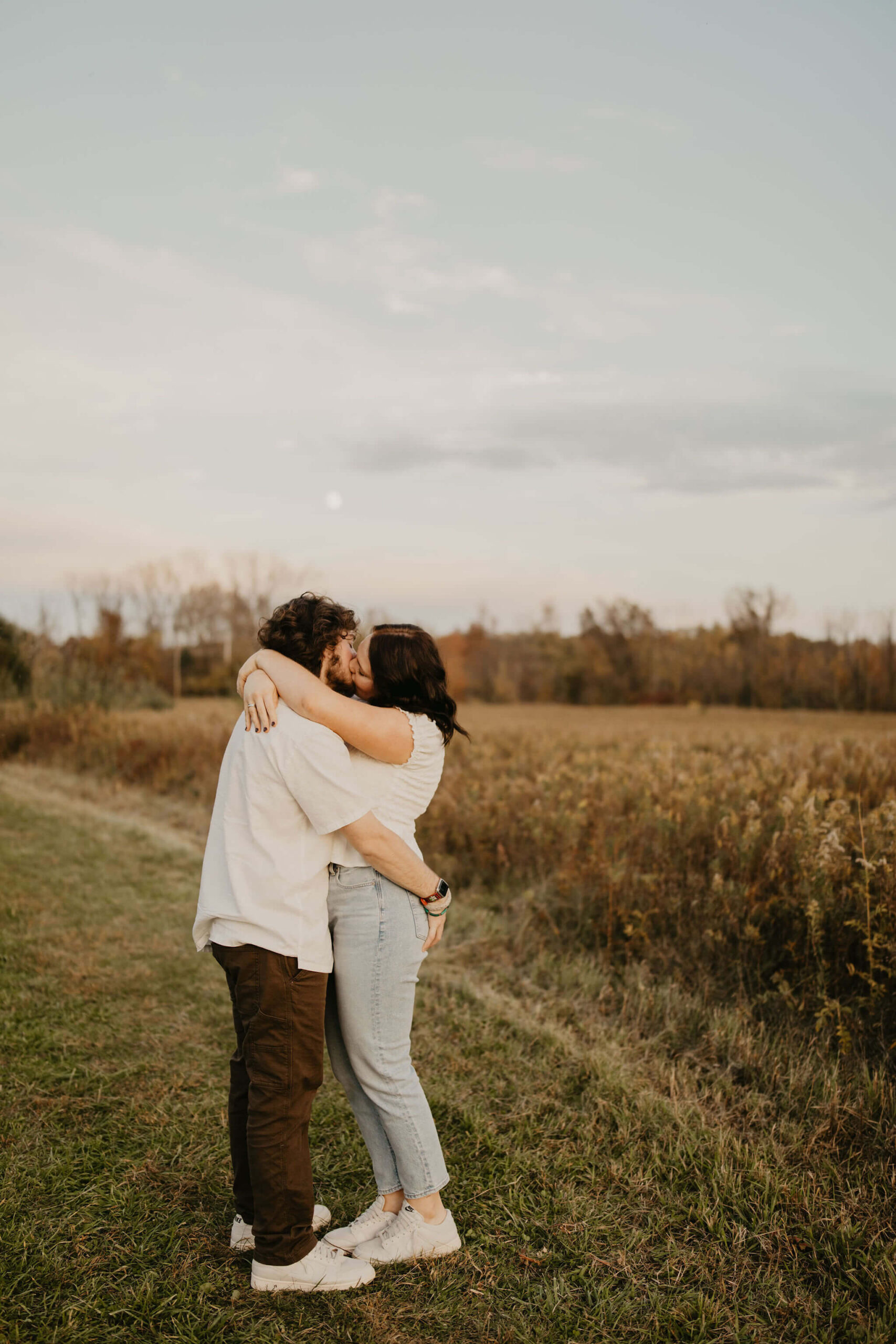 a young couple kissing in a field at sunset while the moon rises over them