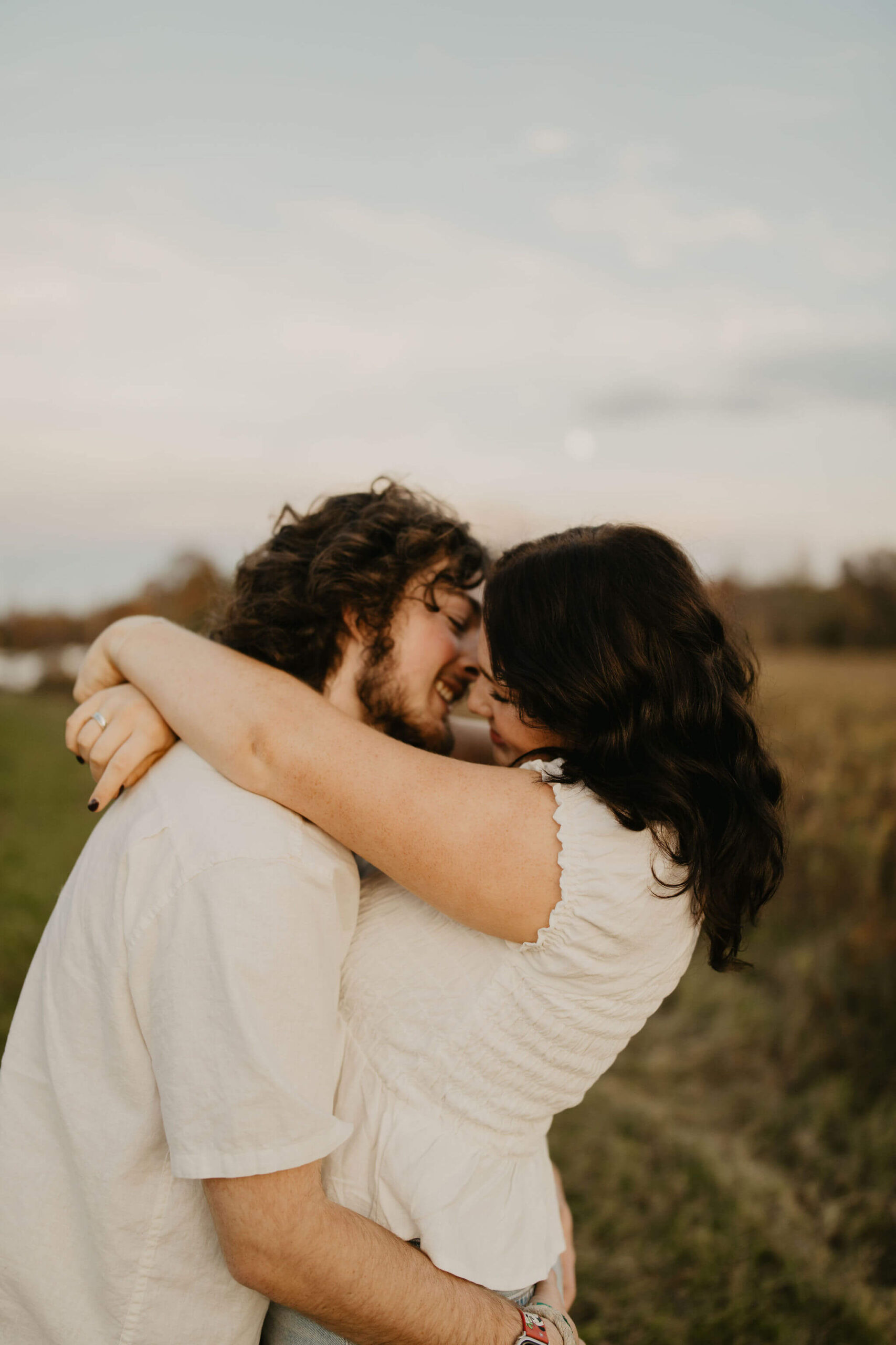 a couple about to kiss, smiling at each other and embracing in a field