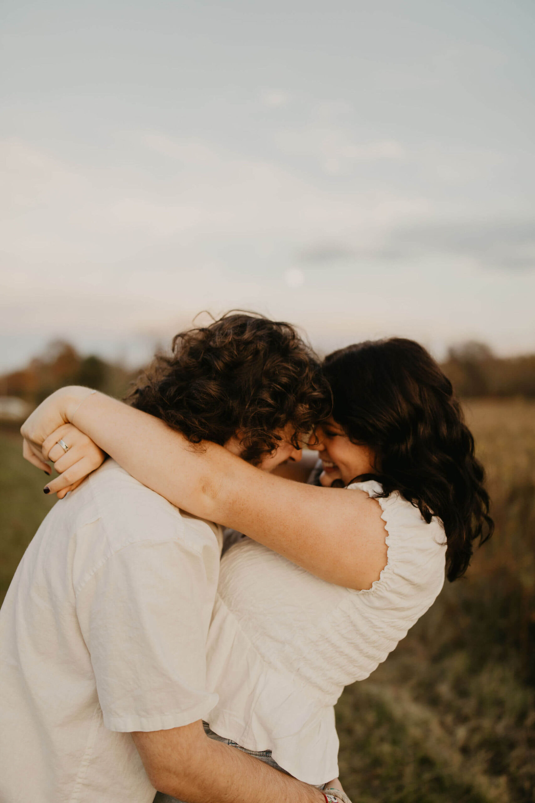 a boy and a girl embracing and giggling in a field at sunset