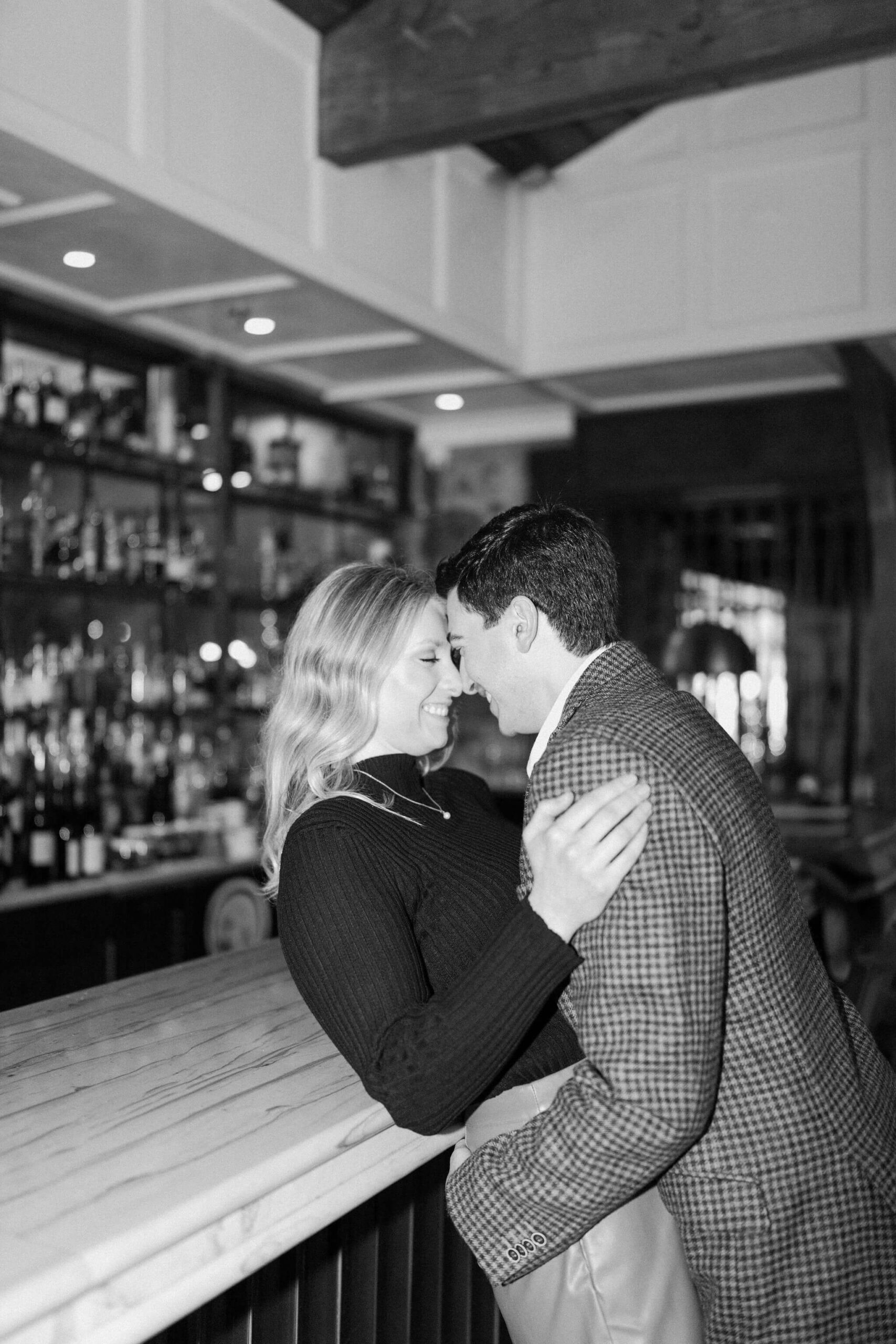 black and white image of a couple at a bar, foreheads leaning together and smiling, with the man leaning the woman back over the bar