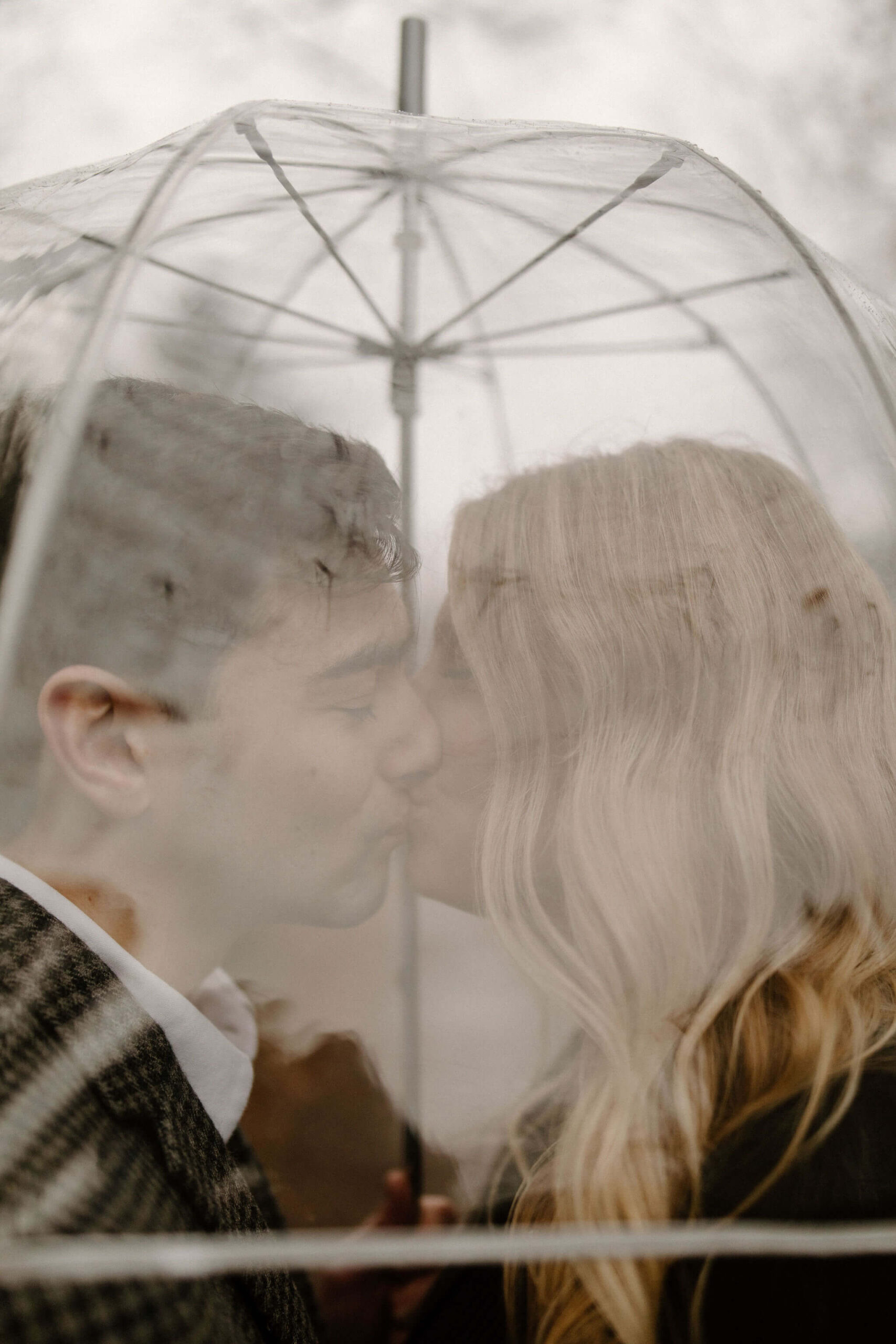 close up image through a clear umbrella of a man and woman kissing inside the umbrella