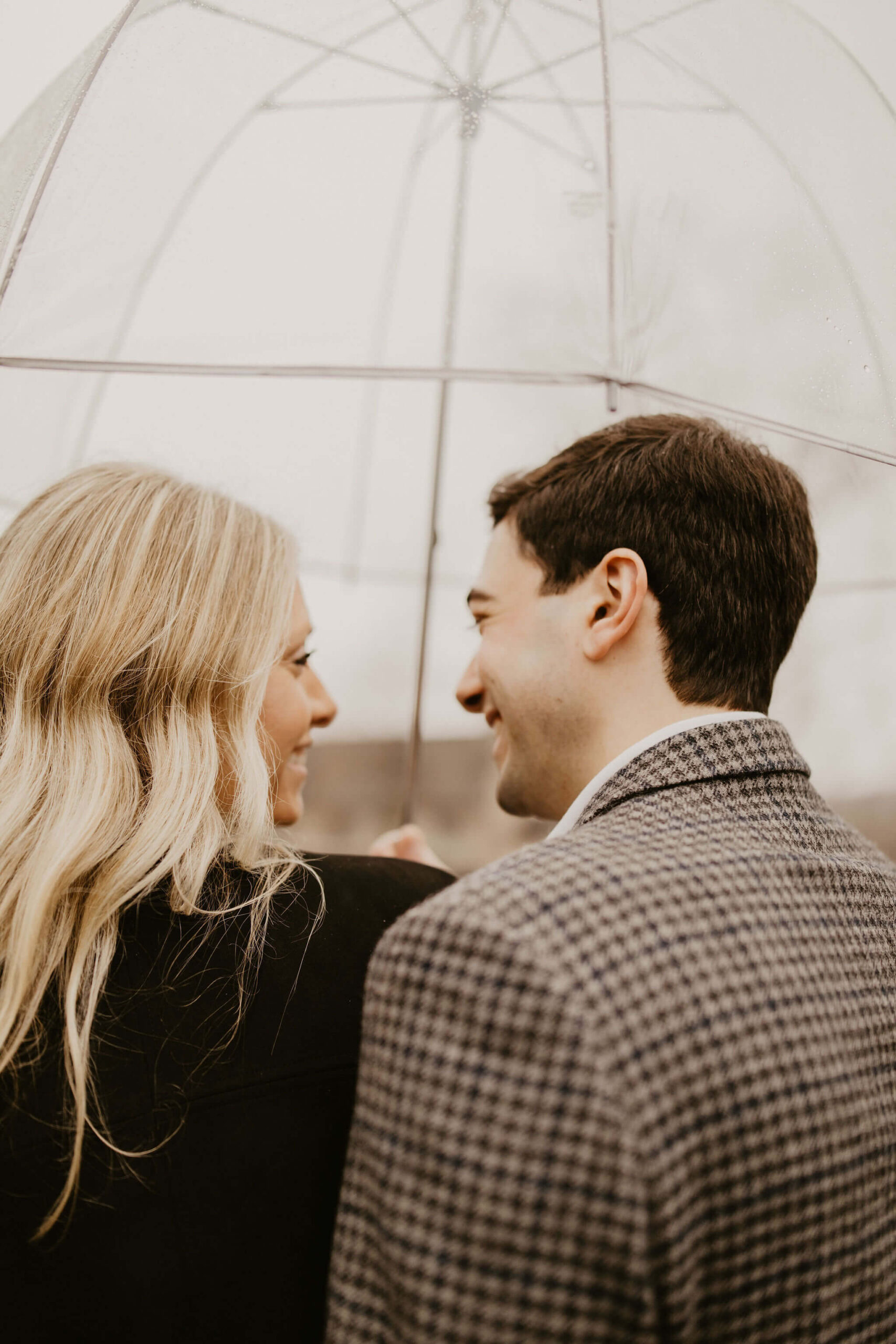 a woman and her fiance smiling at each other under a clear umbrella