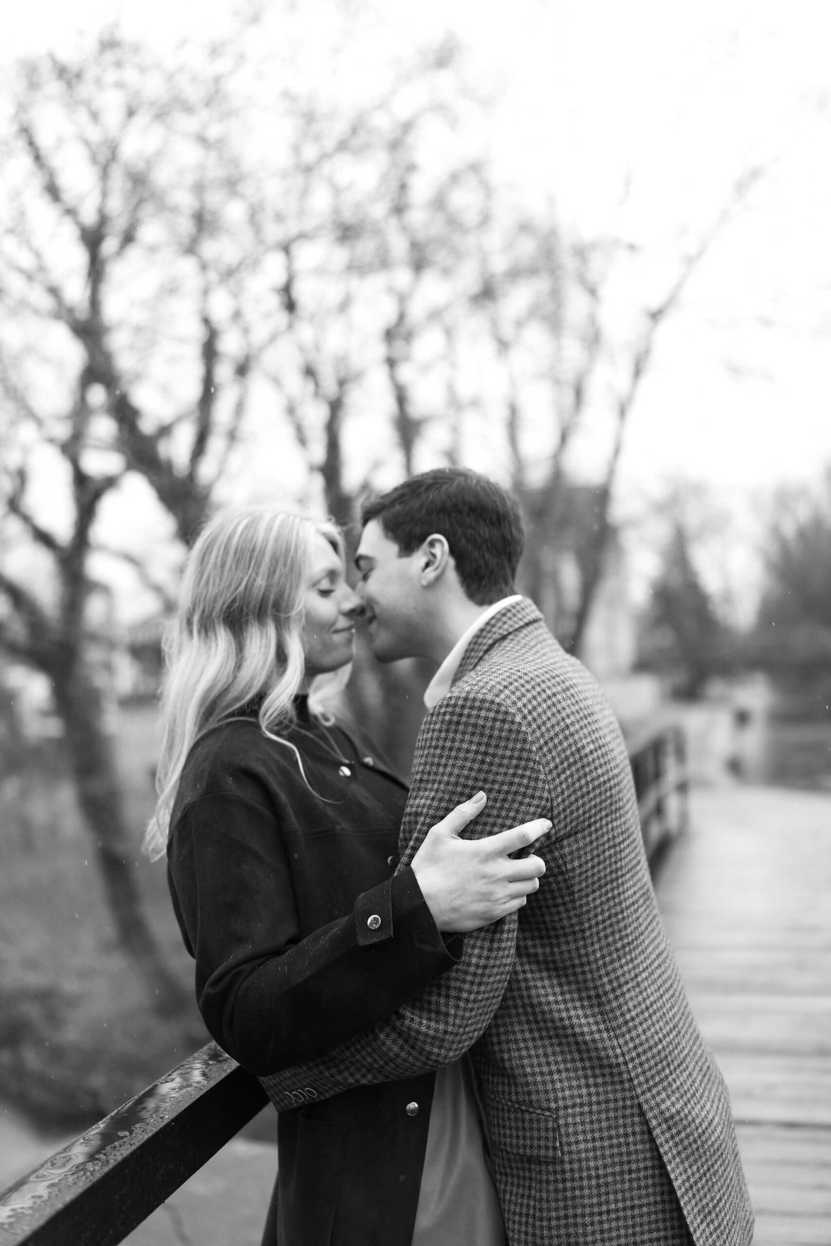 black and white image of a couple about to kiss on a bridge, the man leaning her back into the railing