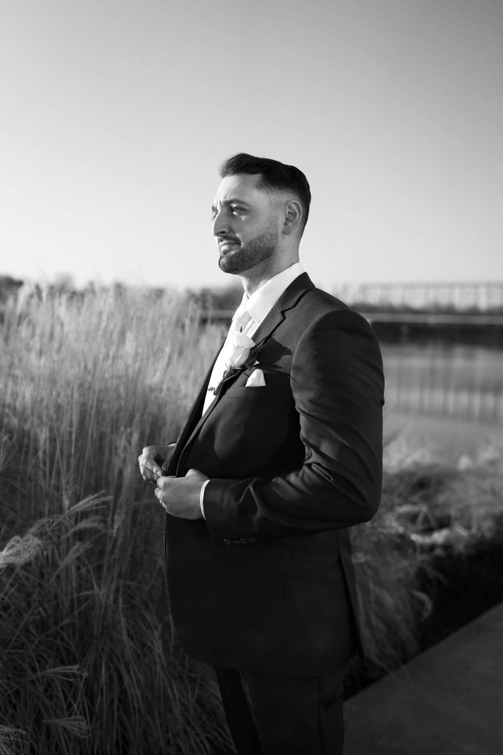 black and white portrait of a groom buttoning his suitjacker