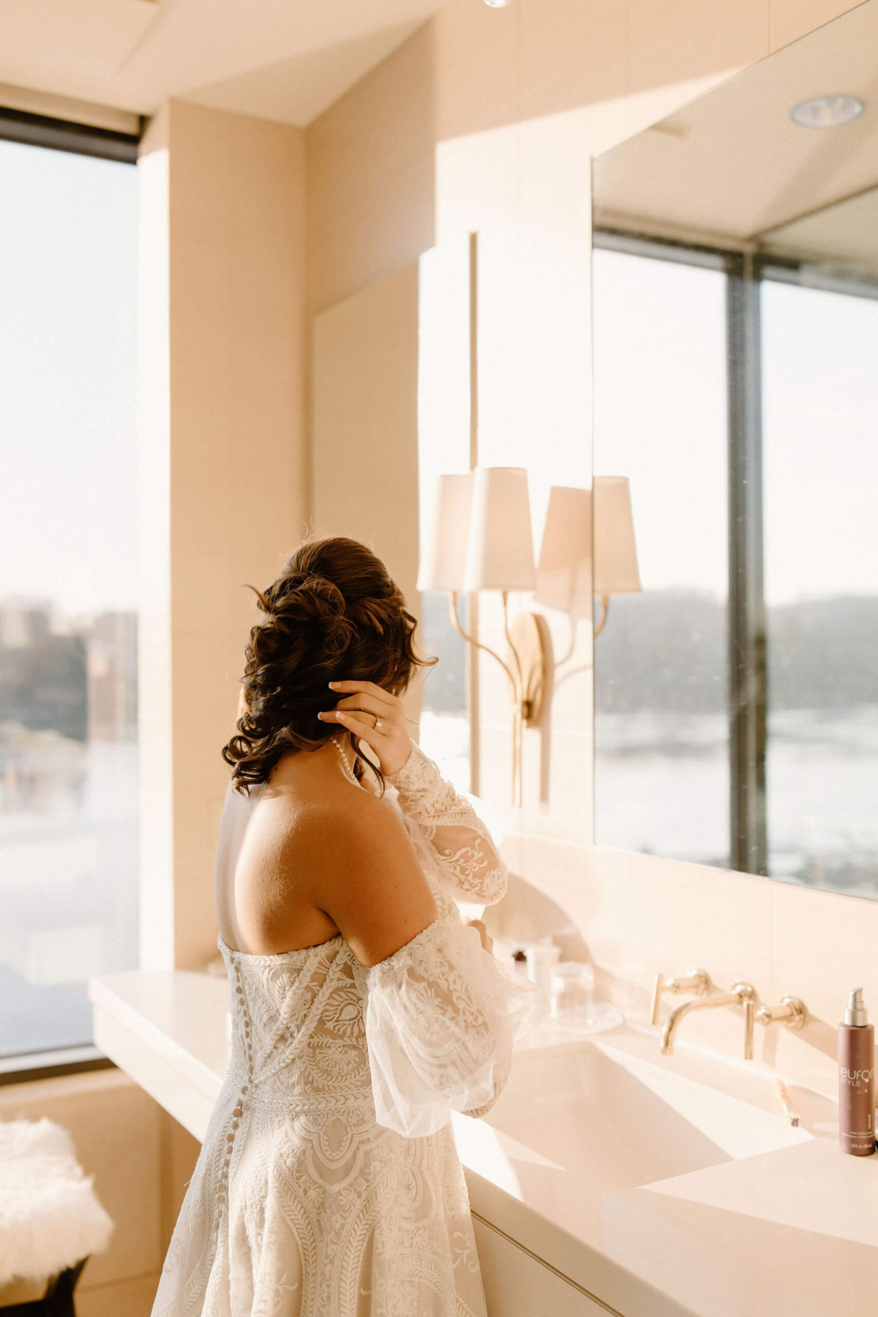 the bride in a bathroom during sunset, fixing her hair