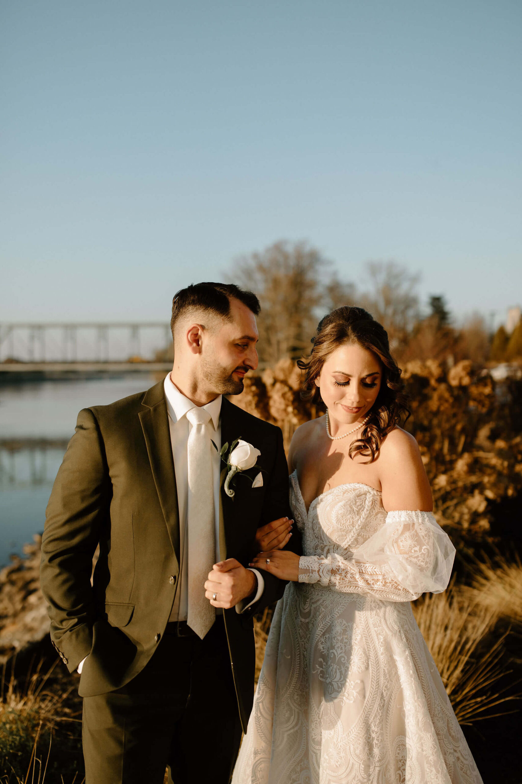 portrait of a bride (brown hair, white dress, looking over her shoulder away from the groom) and groom (brown hair, green suit, looking lovingly at the bride)