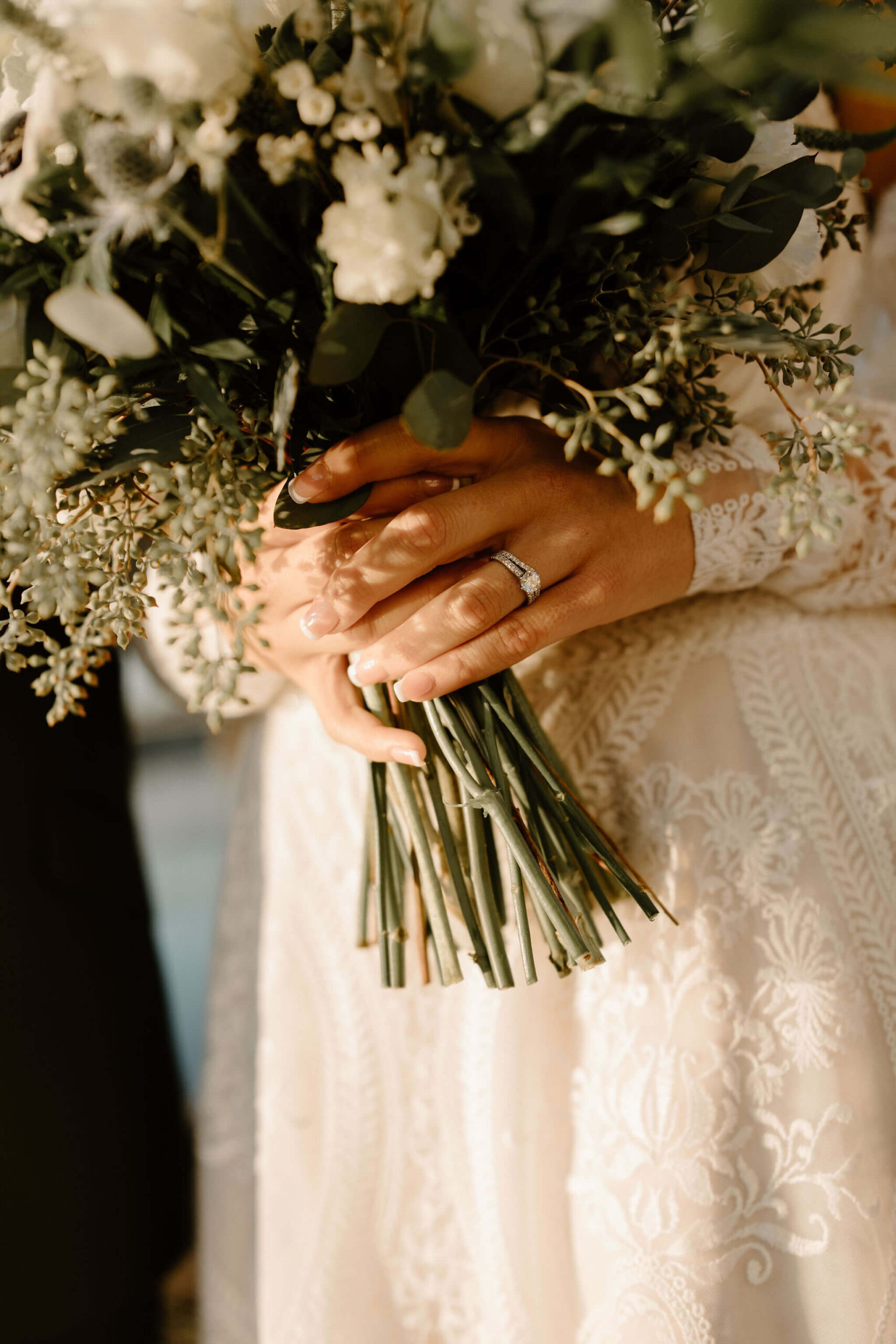 close up image of bride's hands holding her wedding bouquet, focused on her engagement ring and wedding band