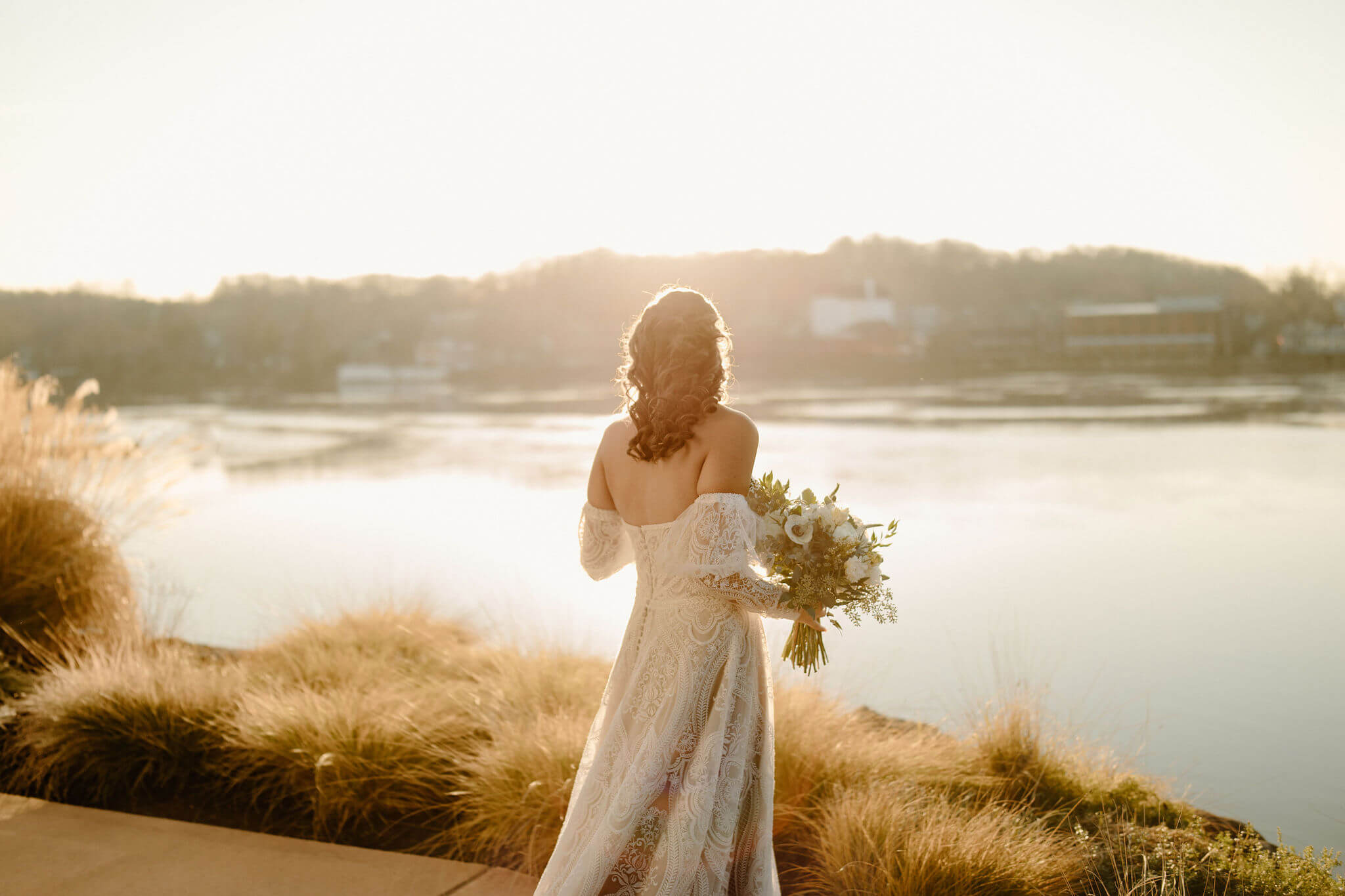 bride looking away from the camera over her shoulder, backlit by the sunset, holding her bridal bouquet