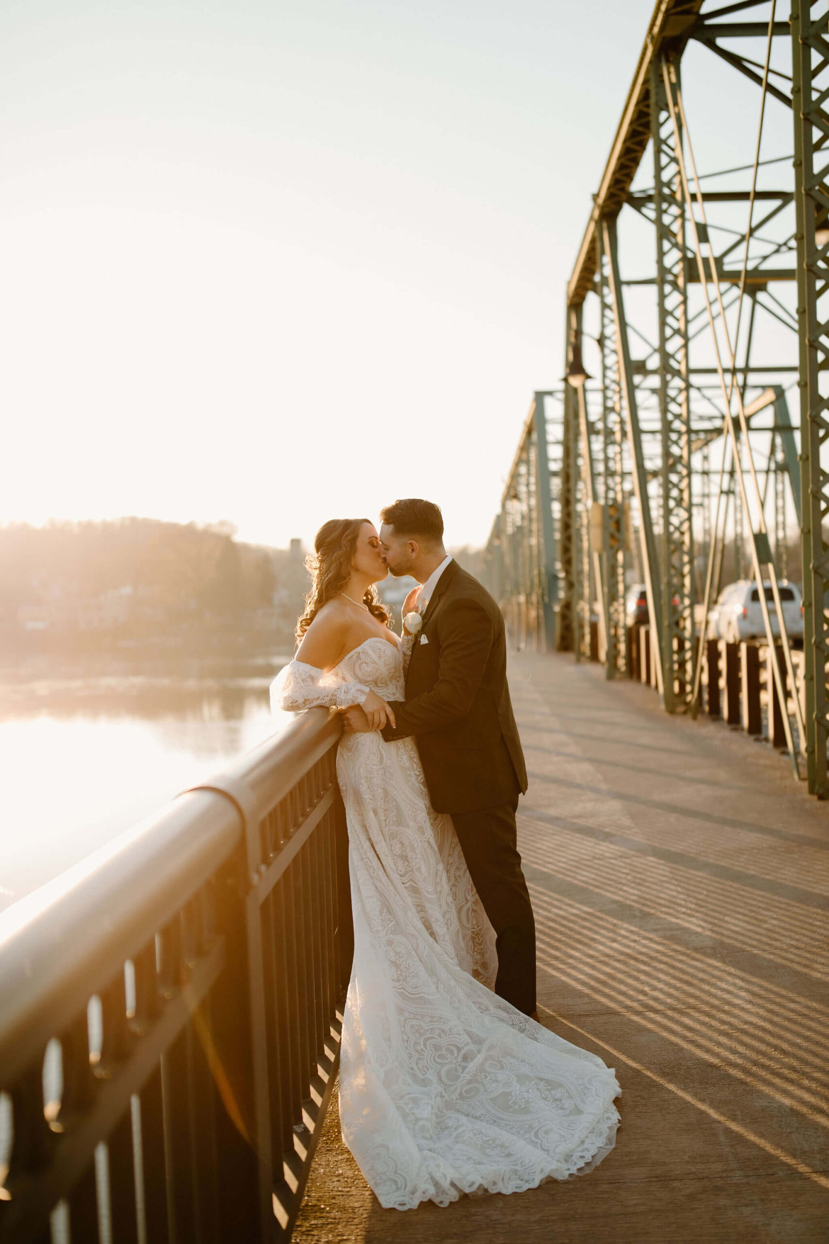 Bride and Groom kissing on a bridge at sunset, overlooking the river