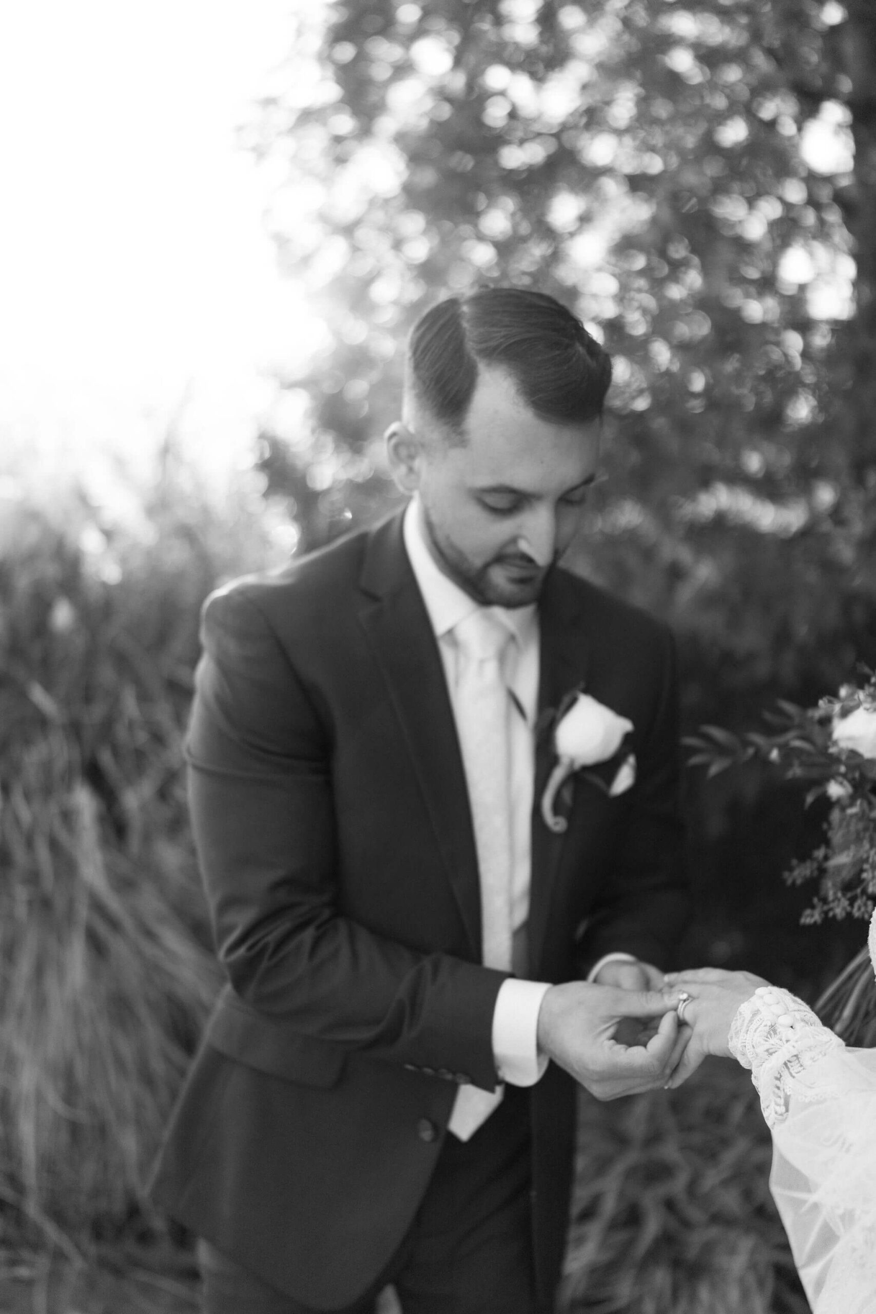 black and white image of a groom straightening his bride's engagement ring on her finger