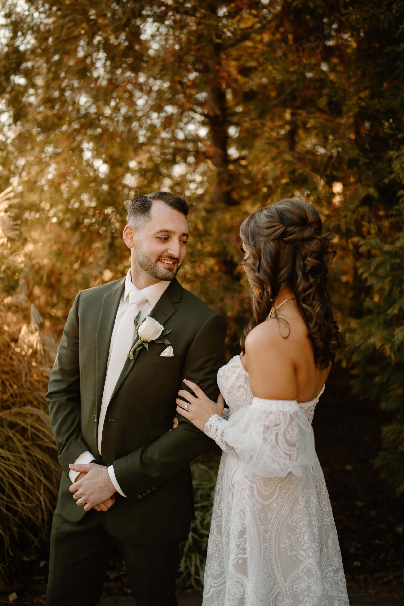 bride (brown hair, textured dress) and groom (brown hair, dark green suit) smiling at each other.