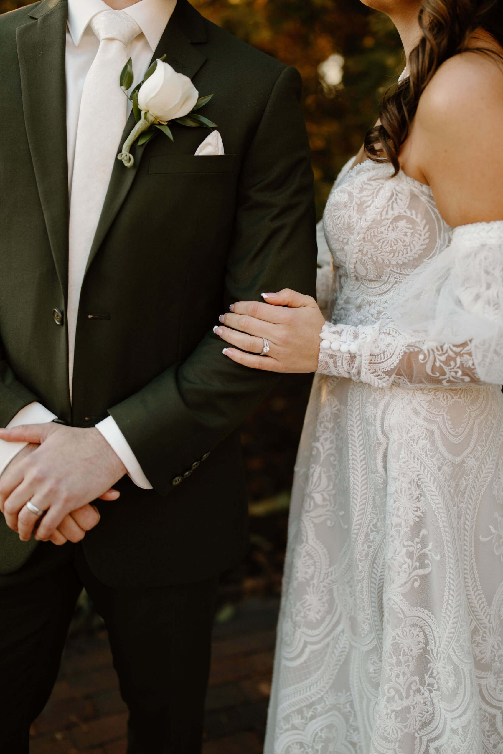 close up image of bride's left hand on groom's left arm, showcasing both of their wedding rings