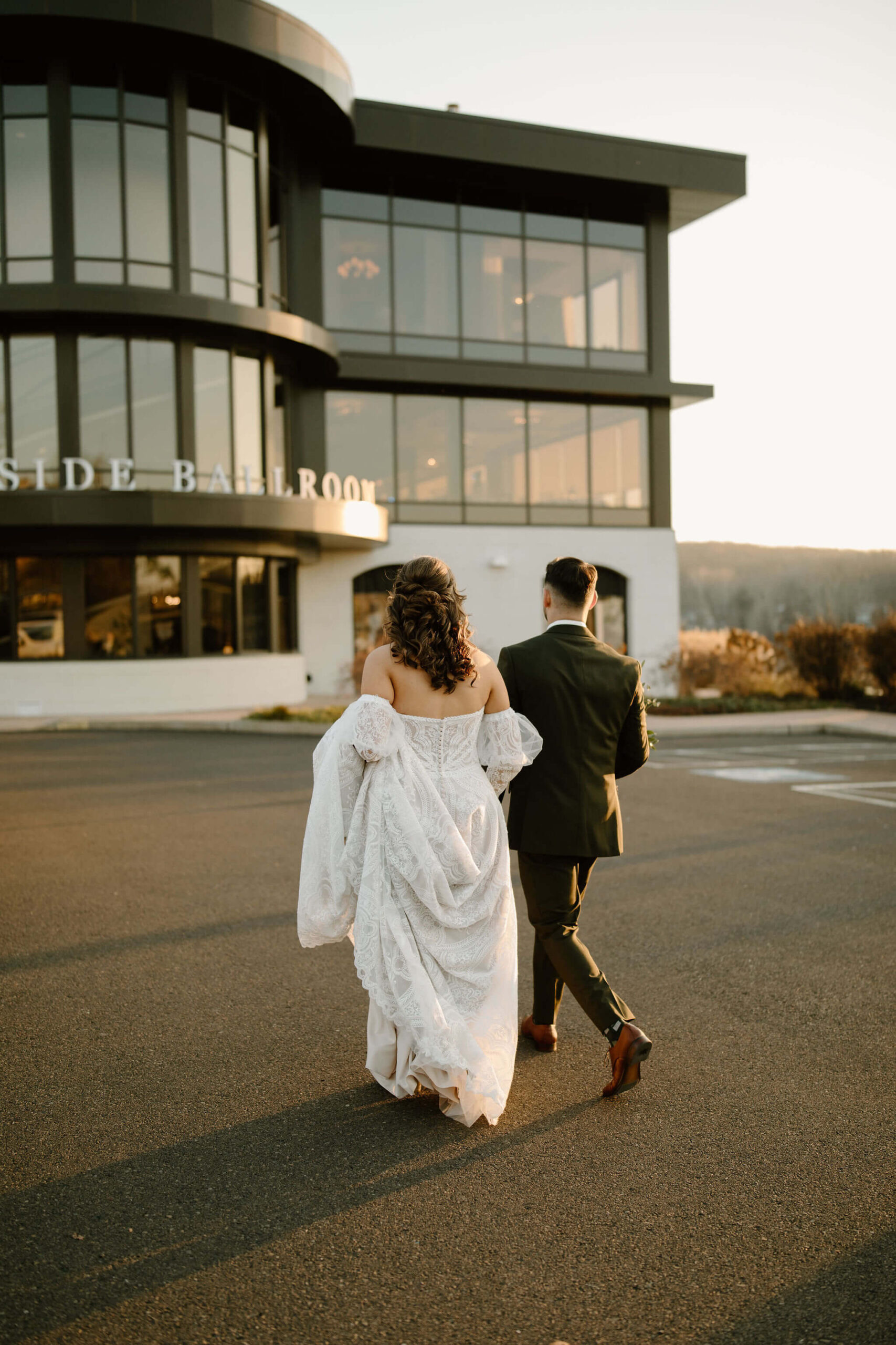 bride and groom walking away from the camera toward their wedding venue at sunset