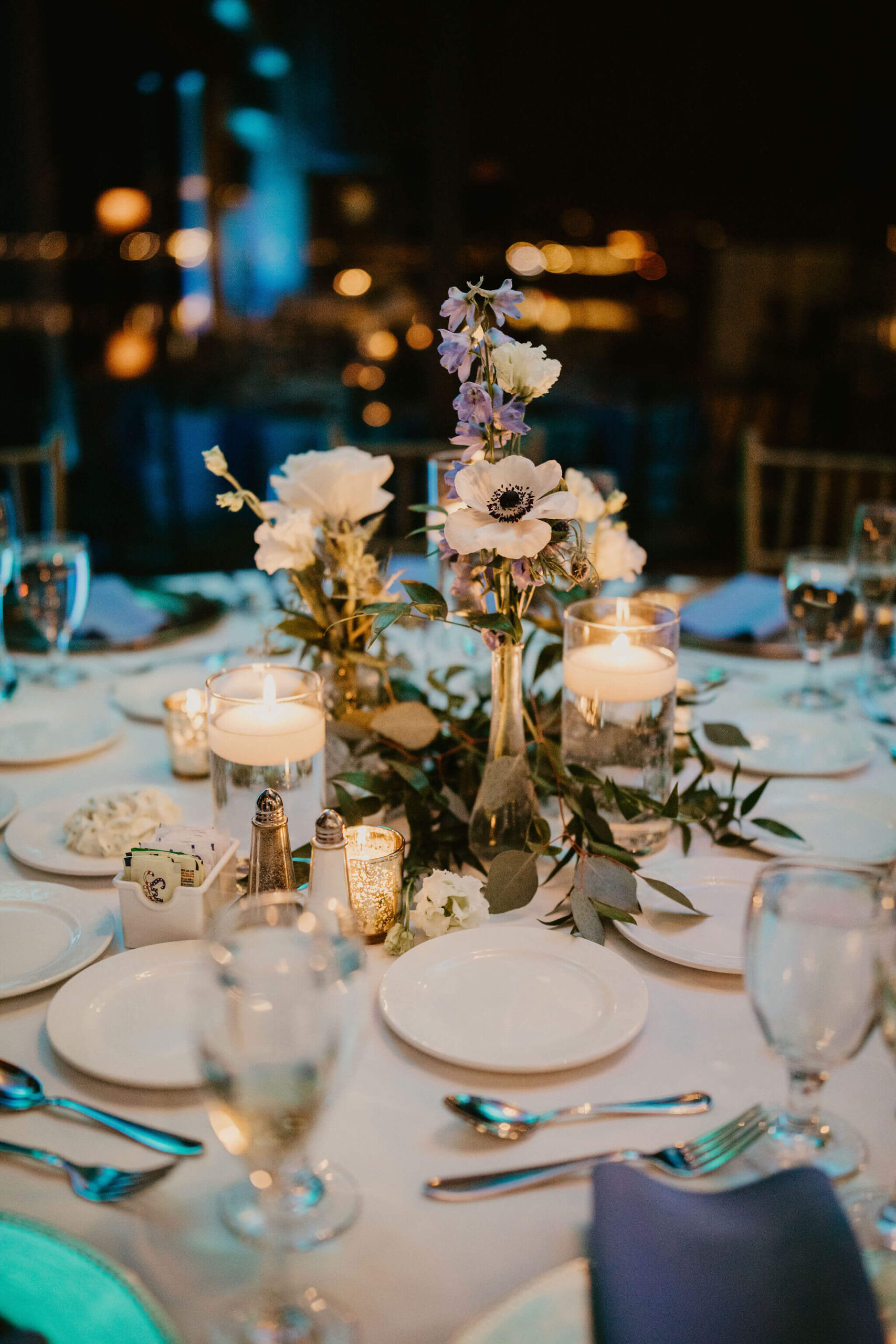 a close up image of reception centerpieces, featuring floating candles and bud vases of white and blue flowers