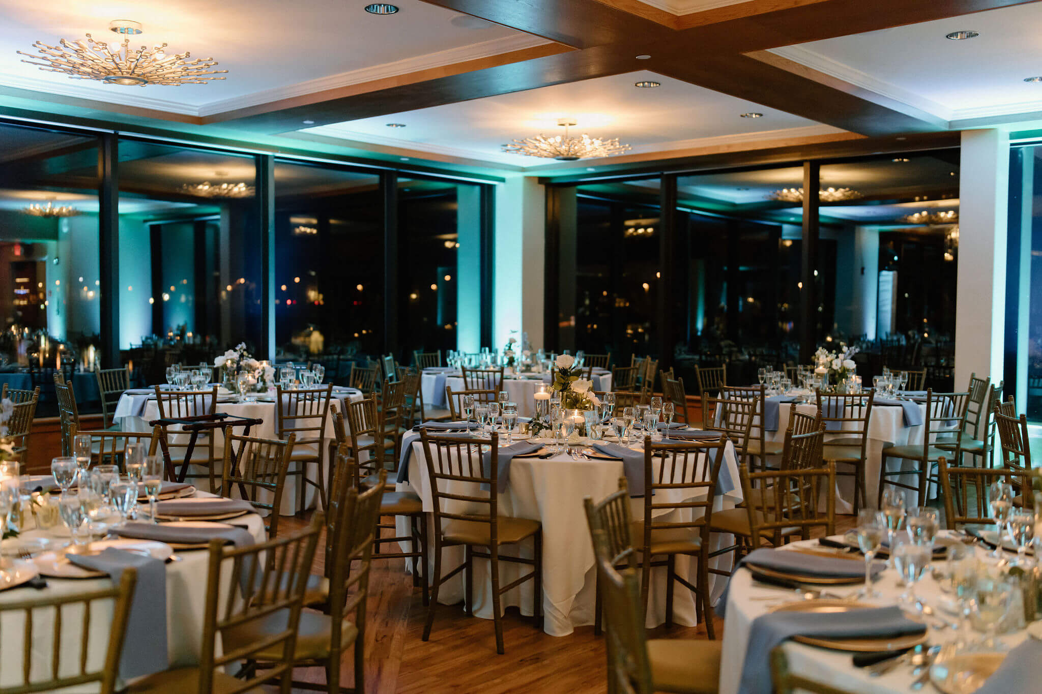 a wide image of round wedding reception tables with blue up-lighting and blue napkins