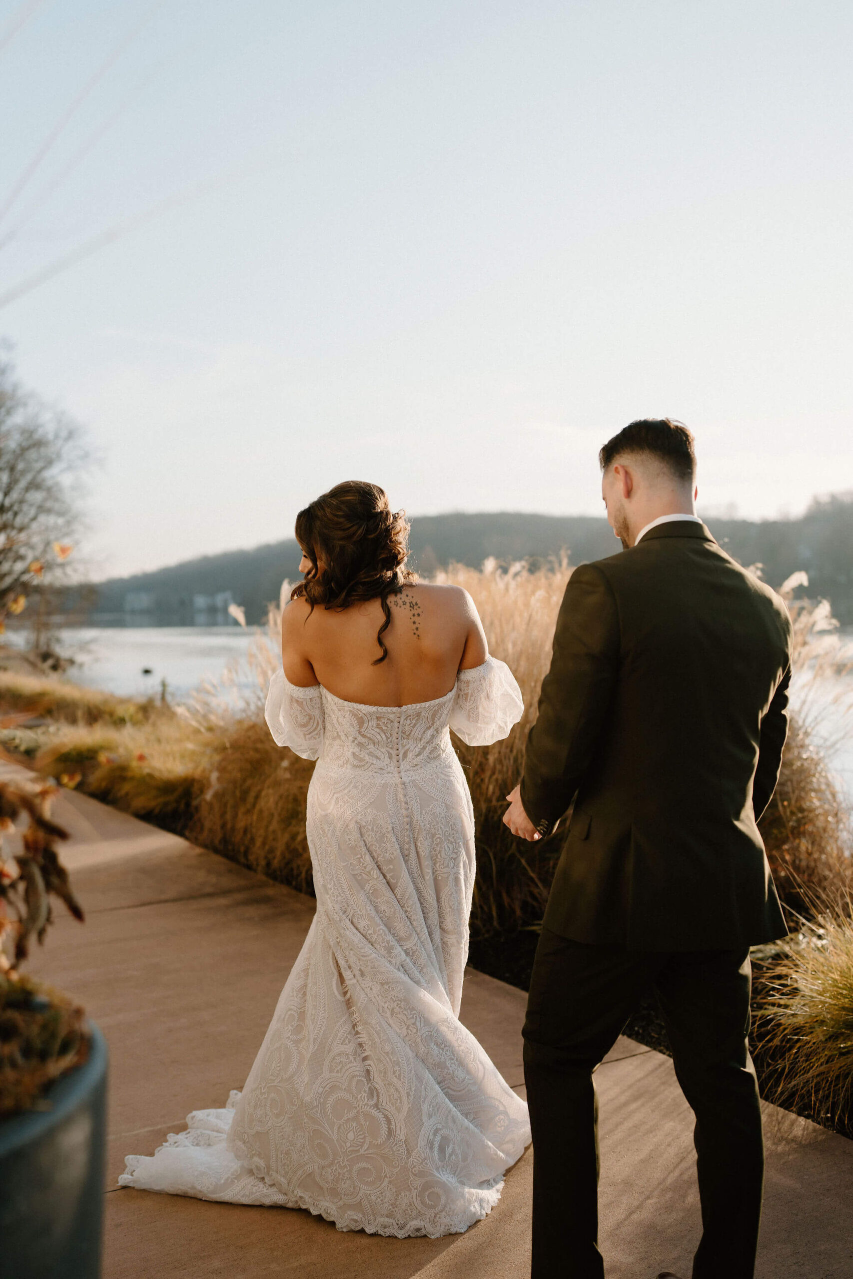 bride (brown hair, textured off-the-shoulder wedding dress) spinning to show her groom (brown hair, green suit) her wedding dress for the first time