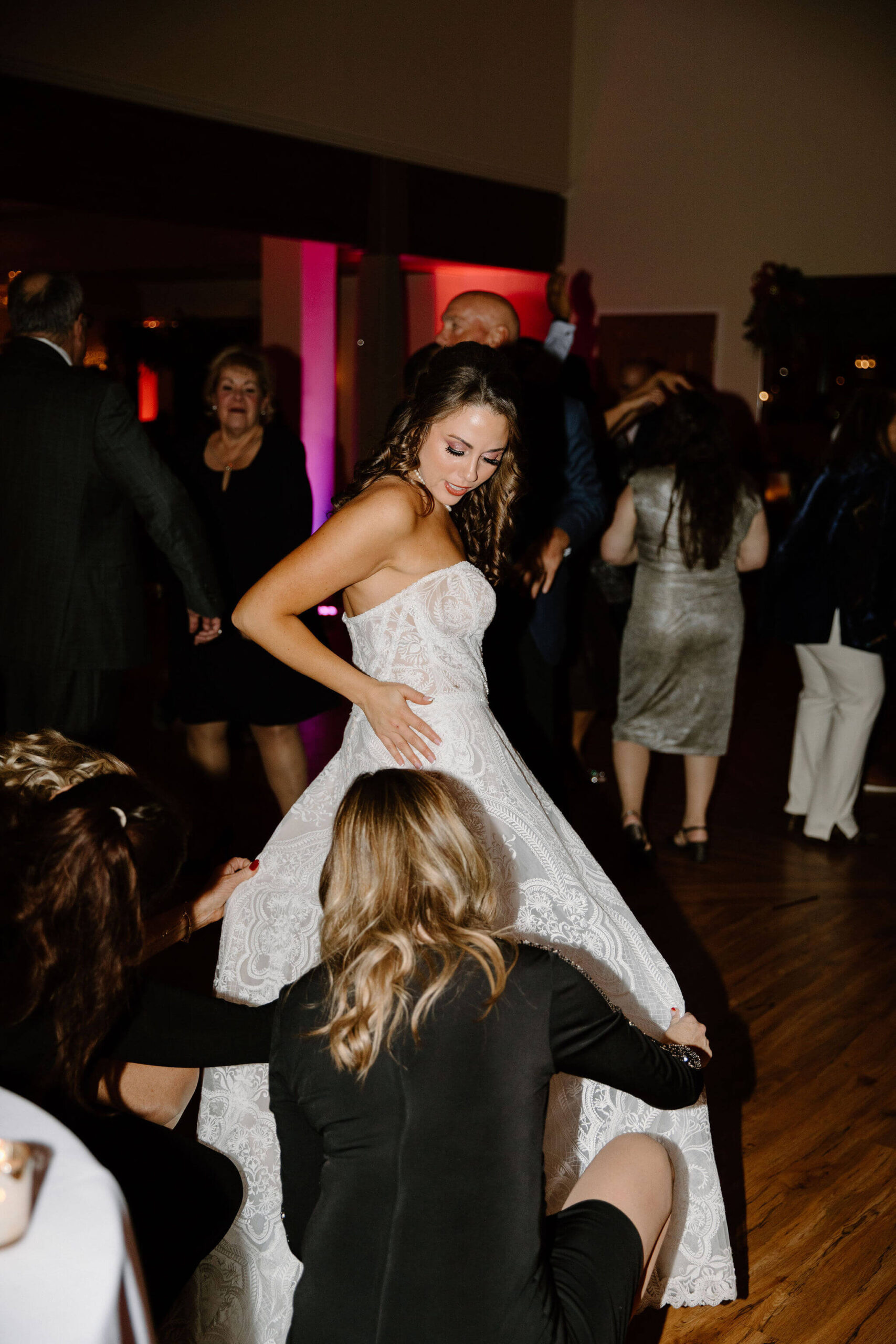 bride looking over her shoulder while her wedding dress is being bustled by friends and family