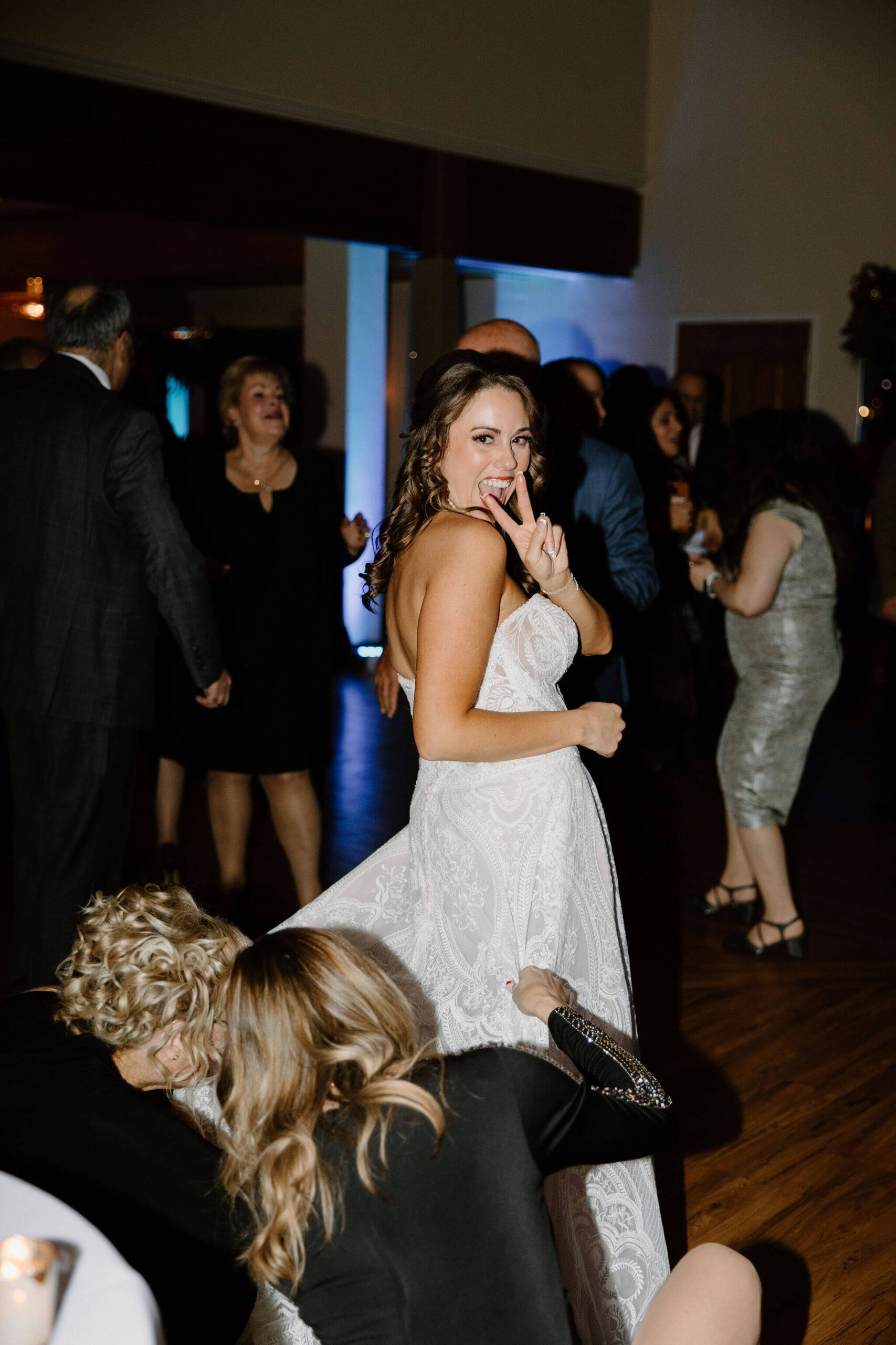 bride looking over her shoulder and giving the peace sign to the camera while her wedding dress is being bustled