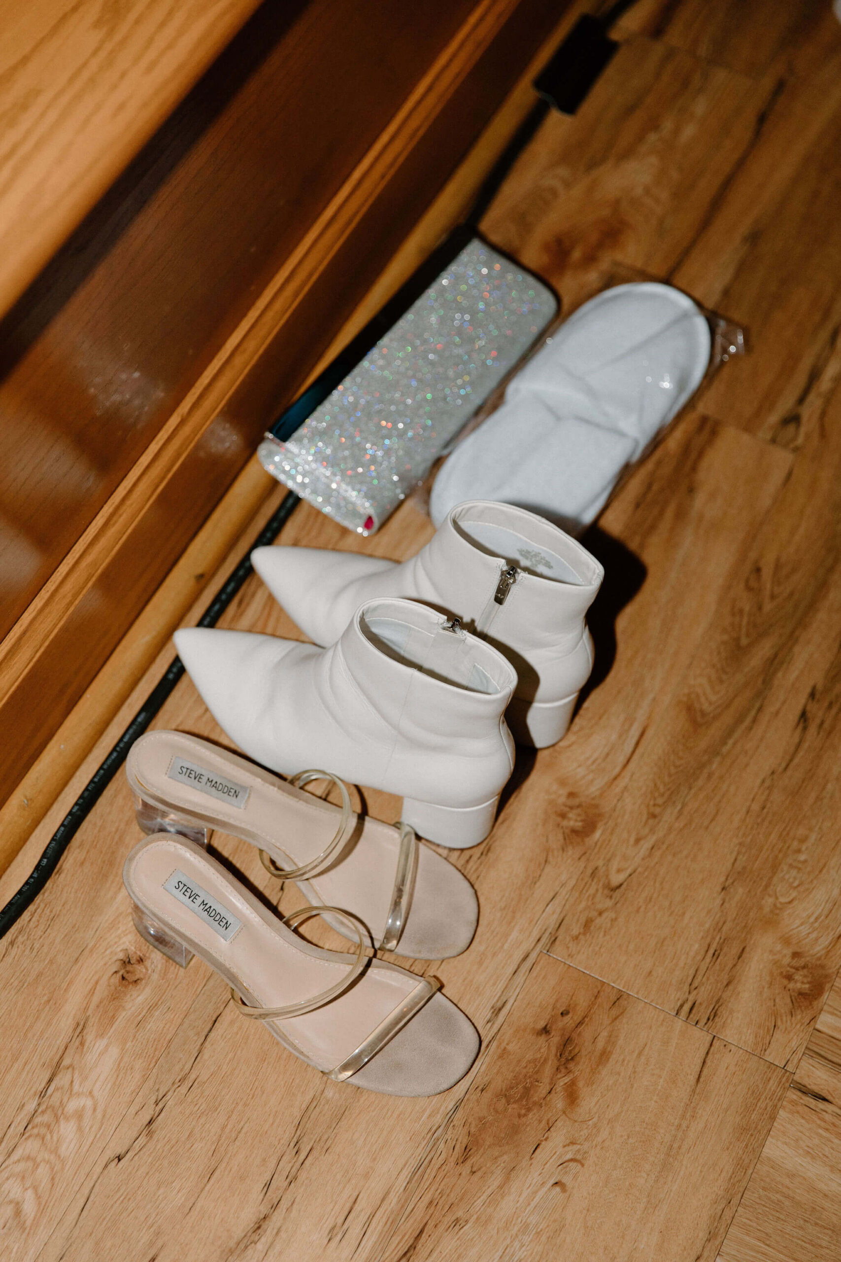 direct-flash image of bride's boots, sandals, slippers, and sparkly silver clutch laying on the floor during a wedding reception