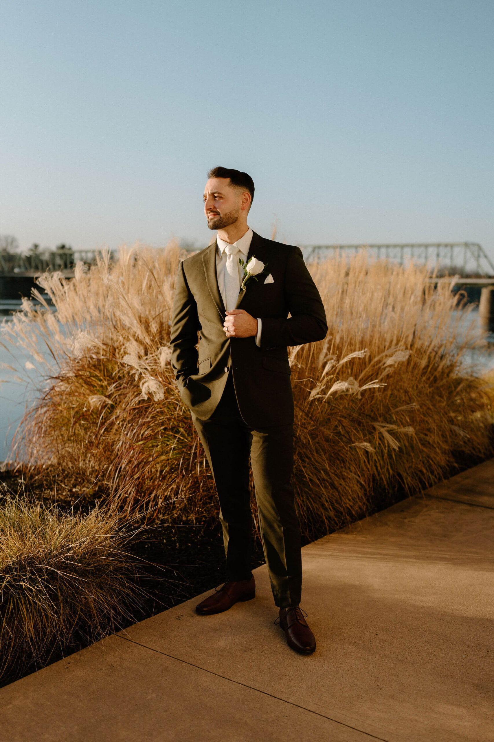 Portrait of a groom on his wedding day (brown hair, dark green suit, looking off camera to the left holding his suitjacket with his left hand)