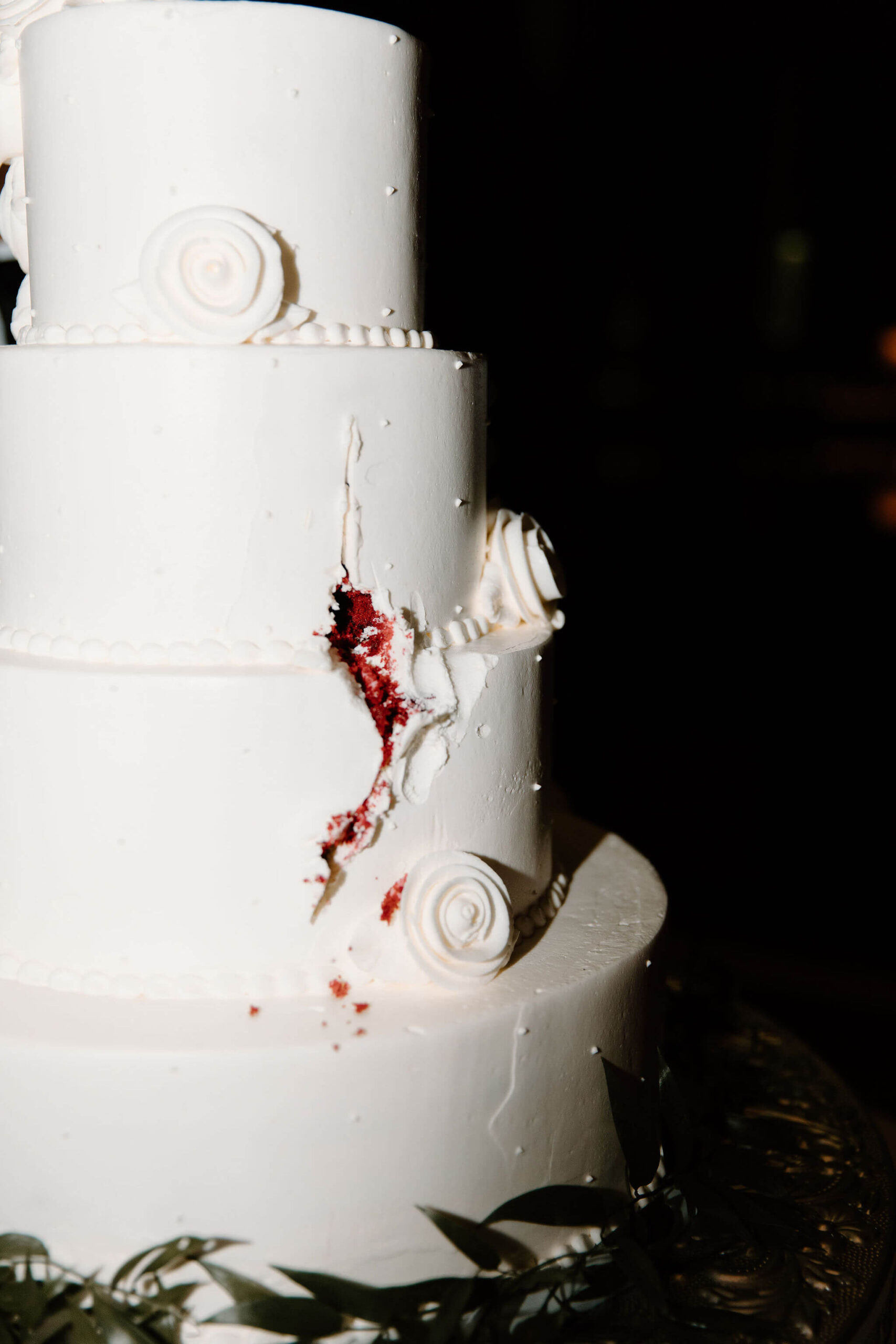 close up direct flash image of a sloppily cut wedding cake with white icing, and a thin, jagged slice of red velvet piercing through the icing