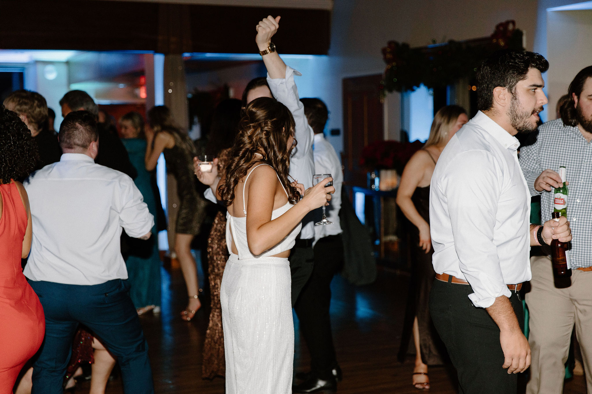 bride (brown hair, white sparkly tank top and sparkly flowy pants) holding a glass of champagne and dancing during a wedding reception